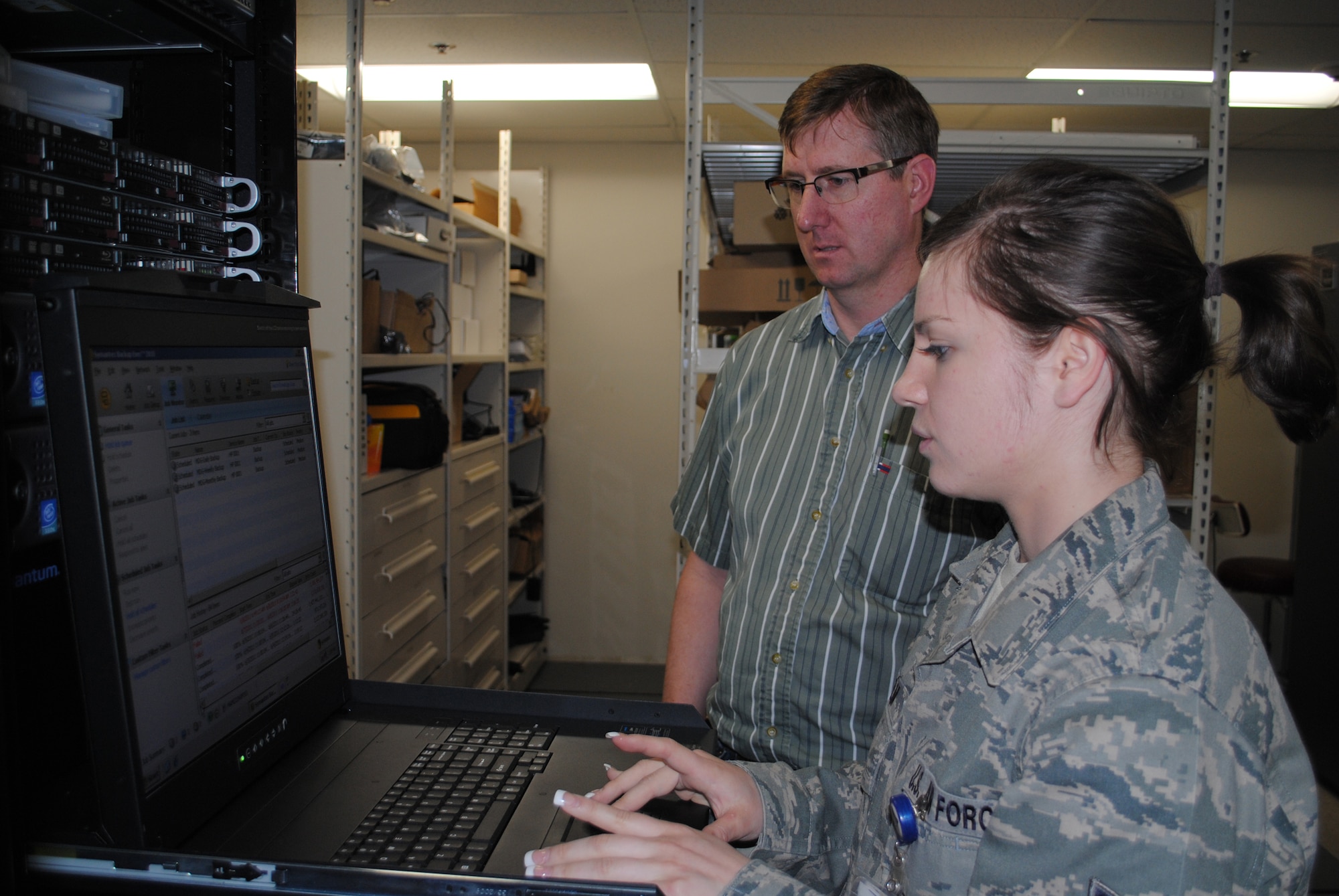 Airman 1st  Class Amy Kelm, 341st Medical Support Squadron computer assistant technician, continues some work on a computer as Kurt Lott, 341st MDSS senior technical support lead, supervises.  Airman Kelm takes on several additional duties along with her every day job requirements.  (U.S. Air Force photo/Airman Cortney Hansen)