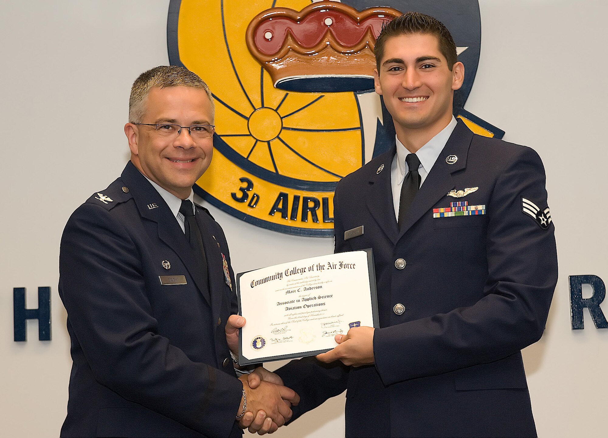 Col. Randal L. Bright, 512th Airlift Wing commander, presents Senior Airman Marc Anderson, 326th Airlift Squadron, with an associate in applied science degree June 12 during a Community College of the Air Force graduation ceremony on base. Airman Anderson is a loadmaster who received his degree in Aviation Operations. (U.S. Air Force photo by Steve Kotecki/Released)