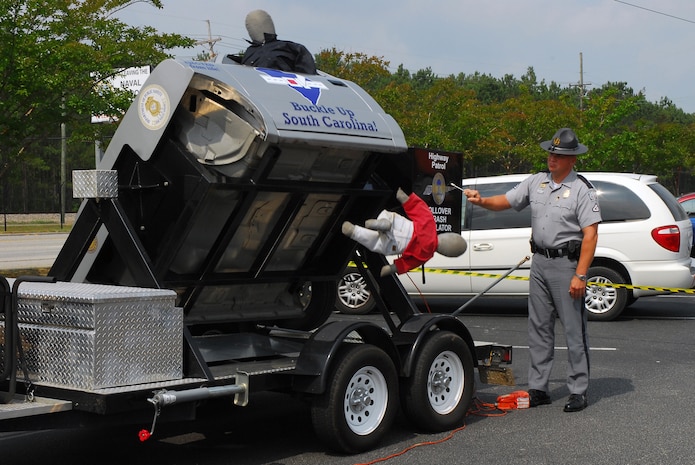 South Carolina Highway Patrol Lance Corporal Bob Beres demonstrates the roll-over crash simulator during a traffic safety event at Joint Base Charleston-Weapons Station June 15. The simulator, which uses crash dummies, demonstrates how individuals not wearing seat belts can be thrown from a vehicle during a roll-over crash at only 12 to 15 mph. (U.S. Navy photo/Machinist's Mate 3rd Class Brannon Deugan) 
