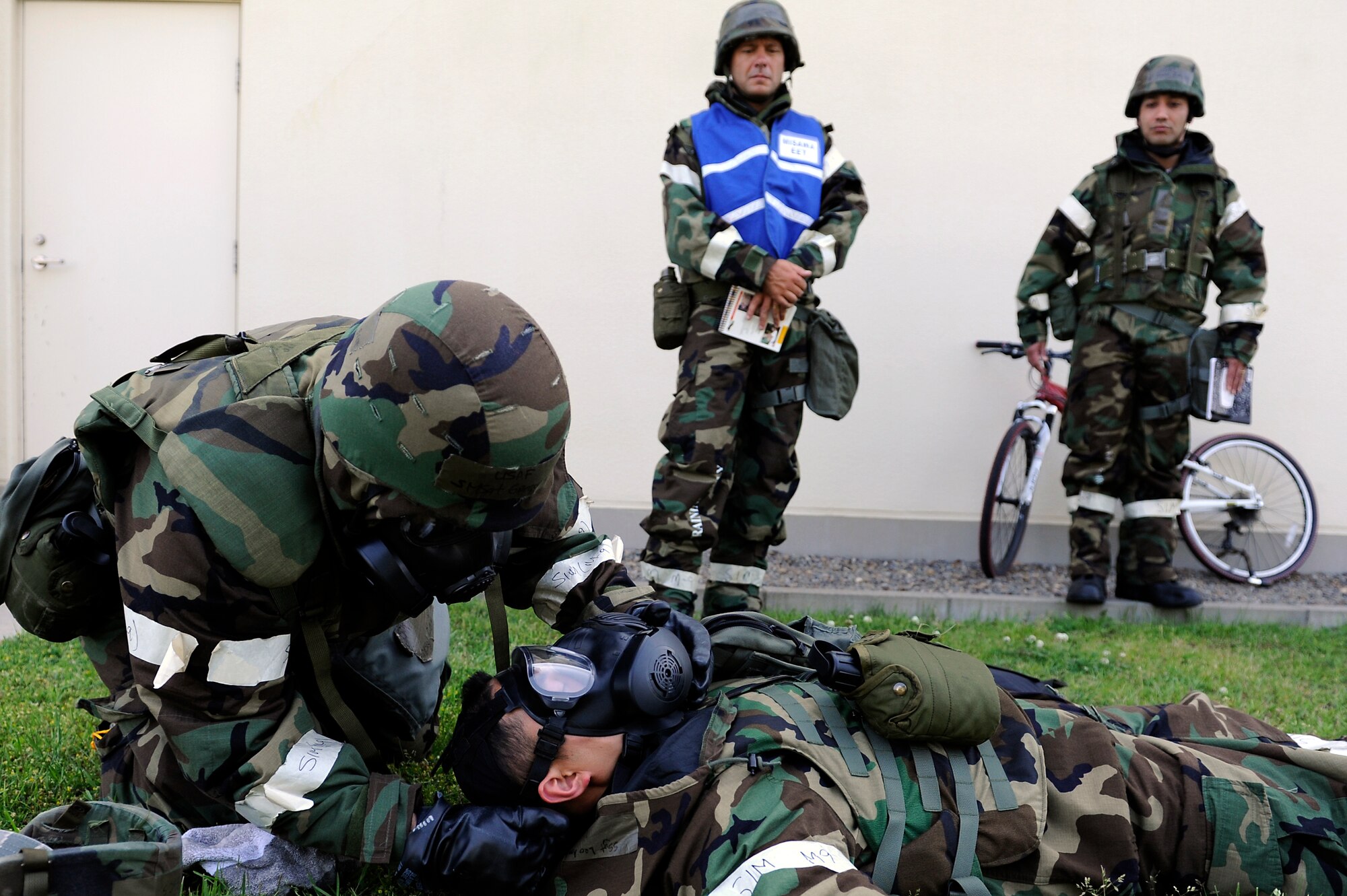 MISAWA AIR BASE, Japan -- Exercise evaluation team members watch as Senior Master Sgt. Gregory Pocaigue, left, 35th Logistics Readiness Squadron, assists a victim of a simulated mortar attack with applying his gas mask during a training exercise June 22. Airmen at Misawa are participating in a week-long exercise designed to test their ability to survive and operate in a combat environment. (U.S. Air Force photo/Staff Sgt. Marie Brown/Released)