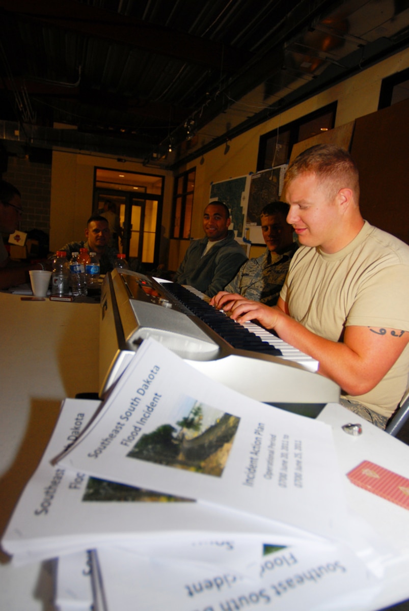 DAKOTA DUNES, S.D. - Senior Airman Zach Gunn,114th Fighter Wing, plays piano and sings songs to help pass the time for the Soldiers and Airmen who would normally be performing levee patrols and quick reaction force duties while taking shelter from a thunderstorm June 20, 2011, in the Dakota Dunes Liberty Bank building. The storm dropped nearly three inches of rain on the already saturated neighborhoods, while the Missouri River continues to rise nearby. (photo by Tech. Sgt. Quinton Young)(RELEASED)