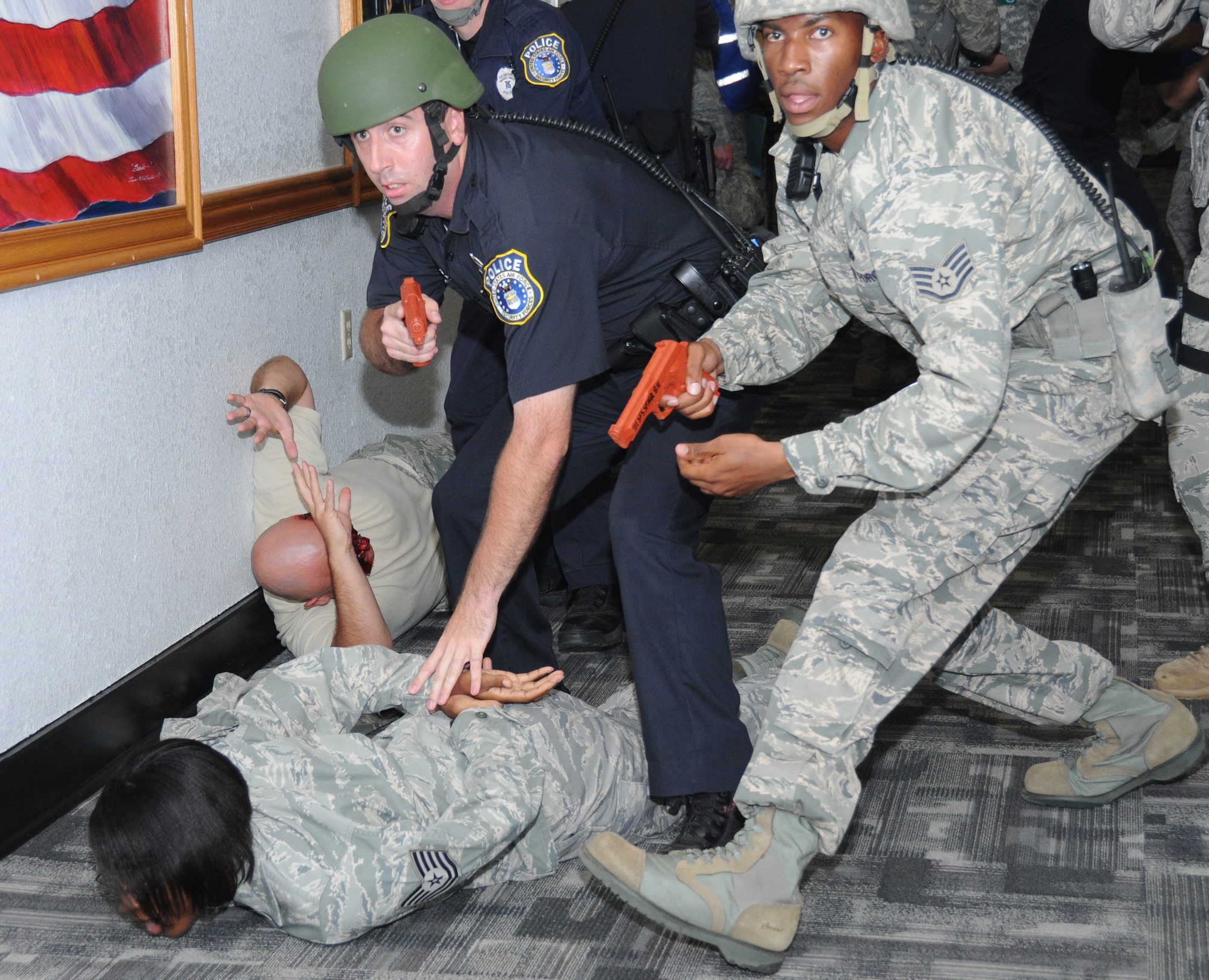 Standing, Benjamin Thomas, left, and Staff Sgt. Jermaine Wilson, 81st Security Forces Squadron, search for a gunman who opened fire at the Airman Leadership School during Tuesday’s active shooter exercise. Sergeant Thomas is questioning Tech. Sgt. Tanya Boyd, injured on the floor in the foreground, about the shooter’s whereabouts and ensuring that she’s not carrying a weapon as her 2ndAir Force co-worker,Tech. Sgt. Jason Reid, lies wounded against the wall. More exercise photos will be published in the June 30 issue of the Keesler News.  (U.S. Air Force photo by Kemberly Groue)