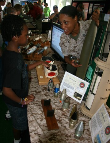 Gunnery Sergeant Tasha Johnson of the Marine Corps Systems Command's Ammunition program office discusses the 155mm howitzer round with a youngster during Marine Week St. Louis.