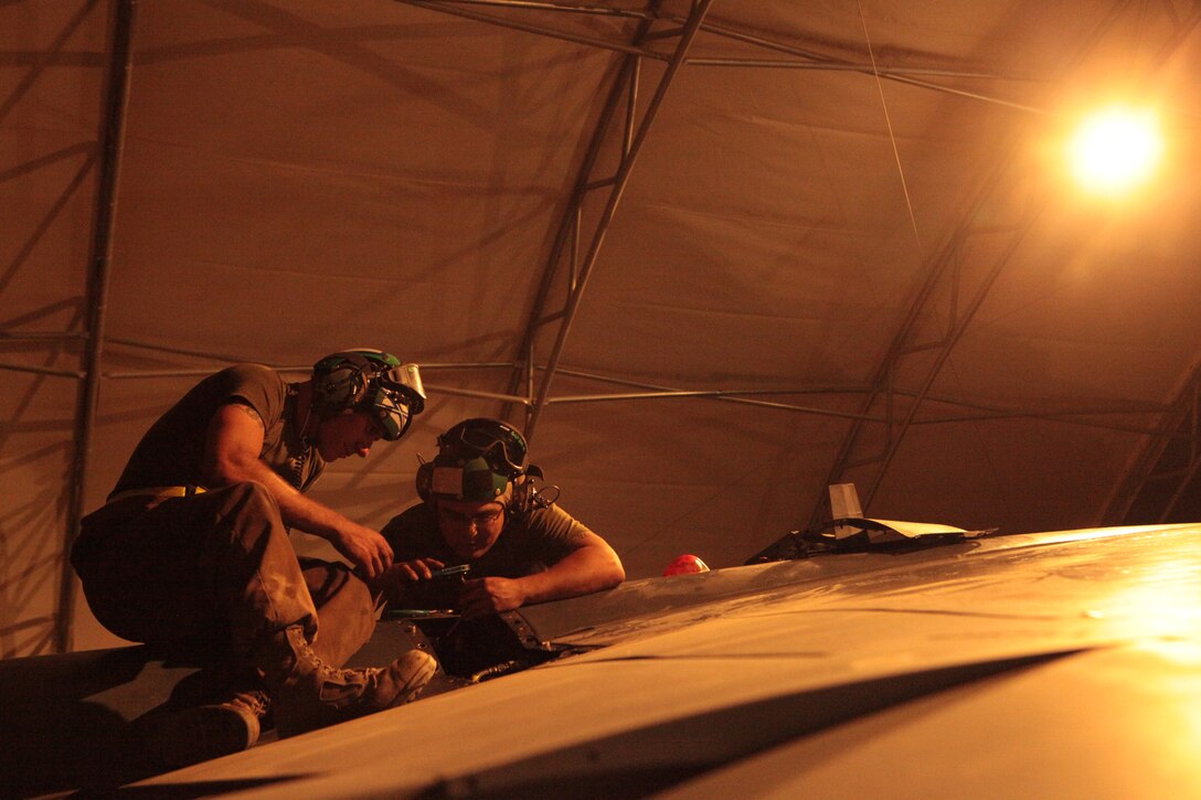 Cpl. Daniel Dye, left, and Cpl. Pedro Guzman, both Marine Attack Squadron 513 avionics technicians, work atop of the squadron’s AV-8B Harriers on the runway of Kandahar Airfield, Afghanistan, with the aid of 1,000-watt lights, June 23. Marine Wing Support Squadron-272 Marines, based in New River, N.C., installed 20 of the lights June 17-21. Previously, the Marines used mobile floodlights to work at night; the new lighting system eliminates such a need.::r::::n::