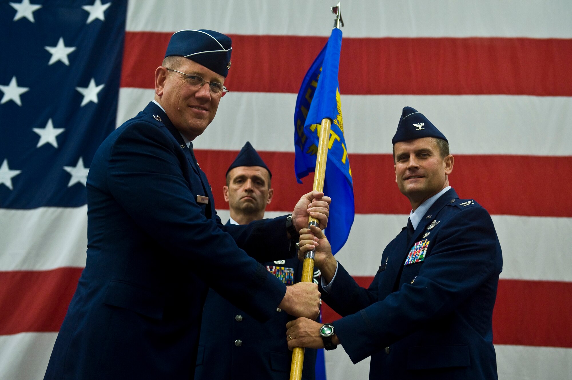 U.S. Air Force Maj. Gen. Bill Hyatt, U.S. Air Force Warfare Center commander, passes the Nevada Test and Training Range guidon to Col. Kenneth Thompson, during an assumption of command at Nellis Air Force Base, Nev., June 21, 2011. During the event, the 98th Range Wing was officially re-designated the NTTR and will remain a direct reporting unit to the U.S. Air Force Warfare Center. The NTTR will continue to operate, maintain and manage the 2.9-million-acre range (42 percent of the land managed by the U.S. Air Force) and 12,000 square miles of military airspace. More than 1,000 military, civilian and contract personnel are assigned to the organization. (U.S. Air Force photo by Senior Airman Brett Clashman/Released)