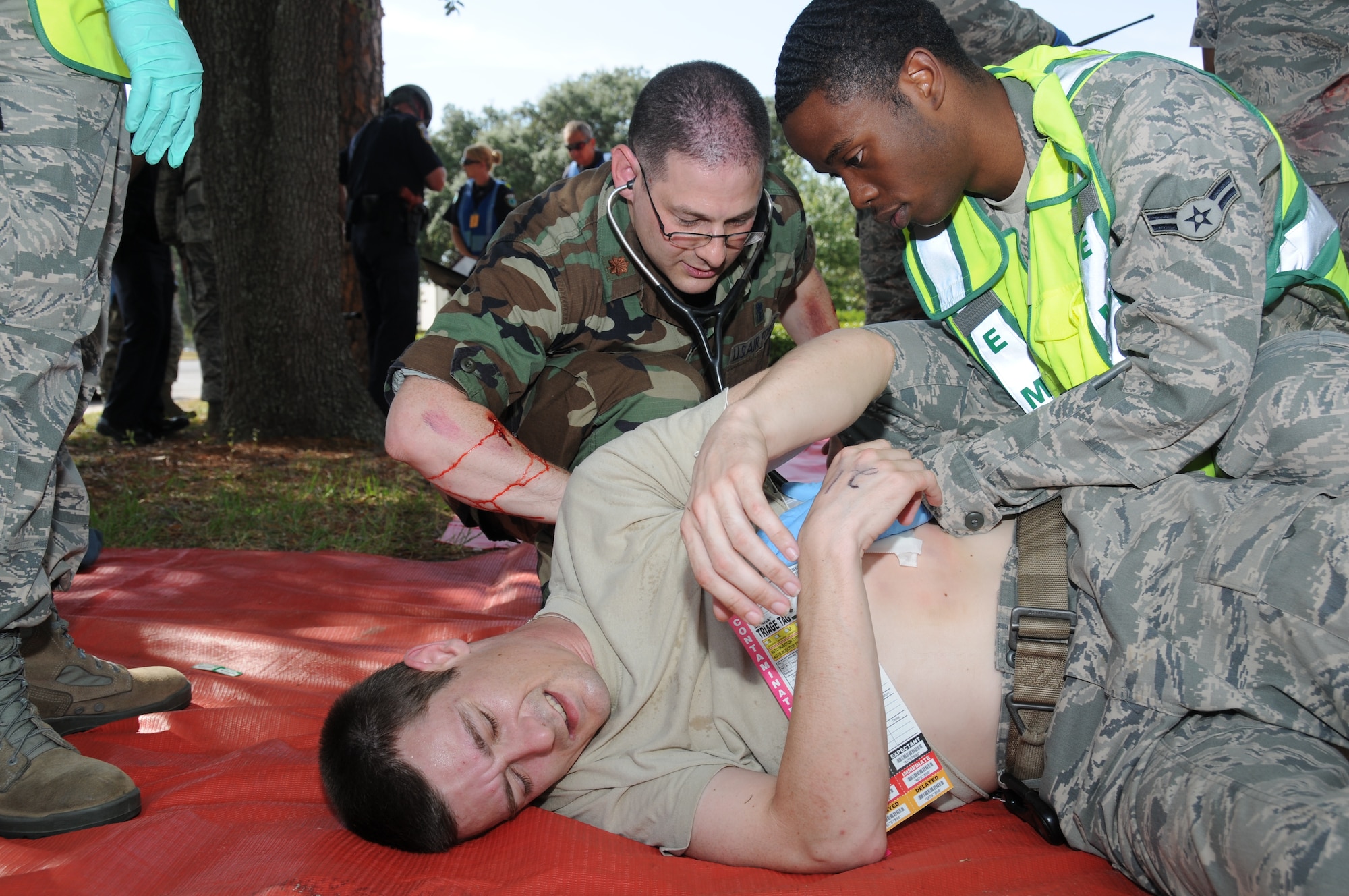 Maj. (Dr.) Allen Stering, left, and Airman 1st Class Rodney Davis, 81st Medical Operations Squadron, assist Staff Sgt. Matthew Bricker, 81st Engineering Installation Squadron, who portrayed one of the individuals that were wounded during Keesler's active shooter exercise, June 21-22.  In the exercise, a lone gunman opened fire at Airman Leadership School, with 12 people killed and 17 injured.  Major Bricker was one of the people "injured" during the shooting spree, but he was able to lend a hand to the medical triage team.  The exercise, conducted by Air Education and Training Command, tested the base's ability to respond and recover from a mass casualty event.  (U.S. Air Force photo by Kemberly Groue)