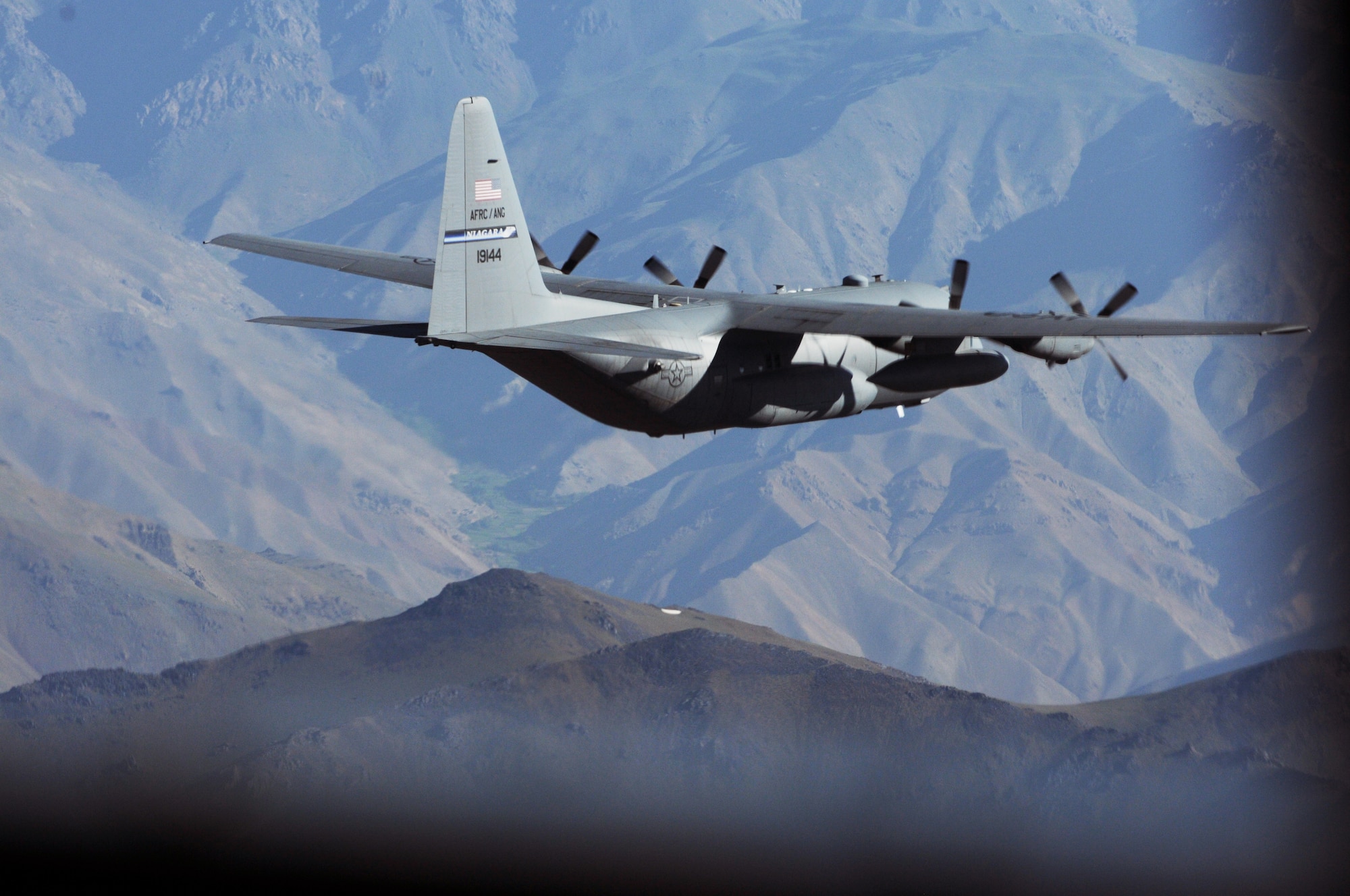 BAGRAM AIRFIELD, Afghanistan -- A C-130 Hercules from the New York Air National Guard flies over mountainous Afghan terrain on its way to delivering much-needed supplies to a forward operating base in Oruzgan Province, Afghanistan, June 22. The New York ANG C-130 flew the airdrop mission in conjunction with another C-130 from the Alaska ANG. Airdrops help mitigate the danger of transporting supplies via convoy. (U.S. Air Force photo by Senior Airman Krista Rose.)