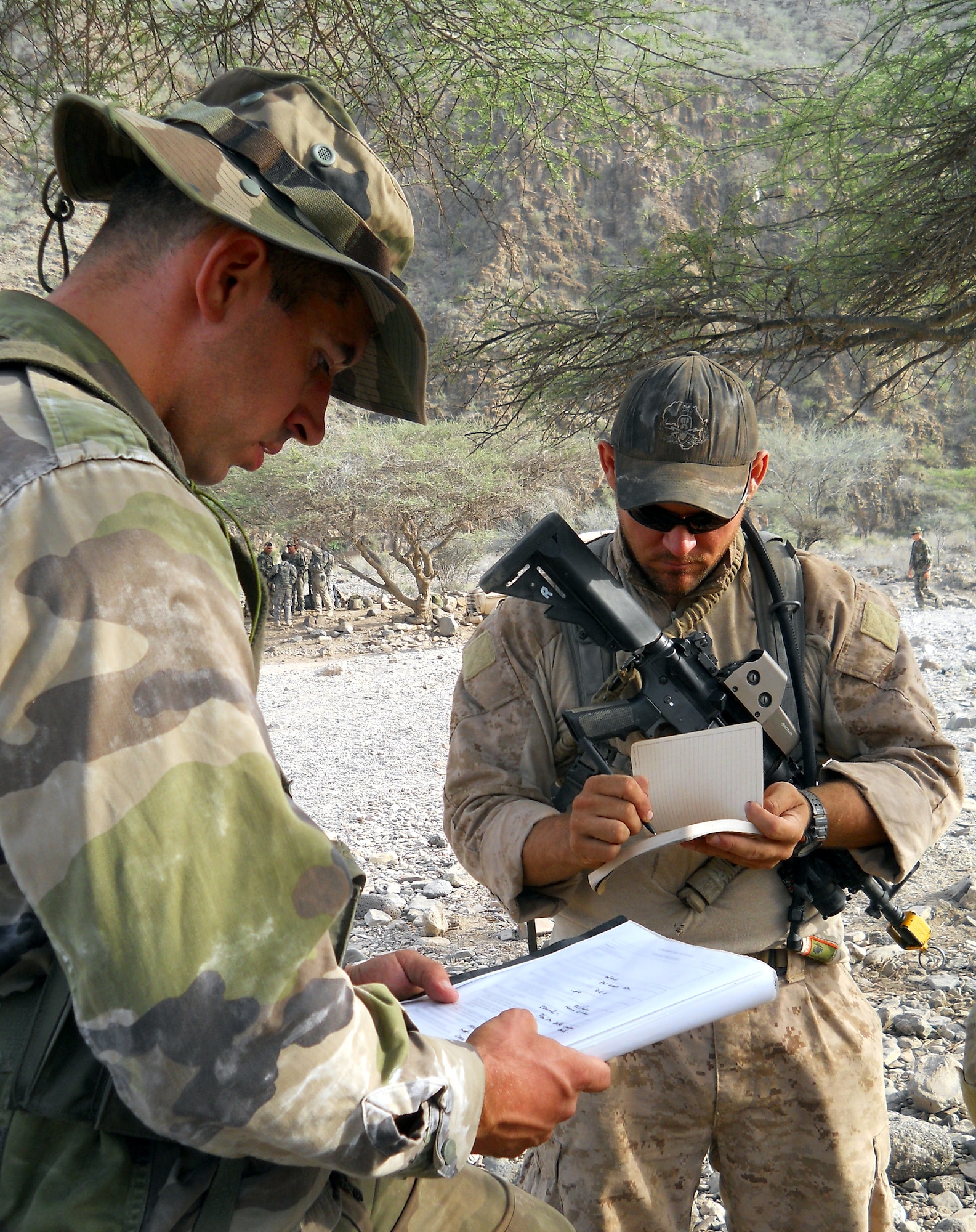 GOUBETTO, Djibouti -- A French Army 5th Marine Regiment member translates a page of desert combat training instruction for U.S. Navy Petty Officer 3rd Class Ryan Donofrio (right), Combined Joint Task Force – Horn of Africa Explosive Ordnance Disposal technician during the course which began May 31, in the Bour Ougoul training area. The 10-day course provided nearly 120 French and 40 U.S. servicemembers with a basic knowledge of field tactics and survival techniques to use within a desert environment. (U.S. Air Force photo by Staff Sgt. R.J. Biermann)