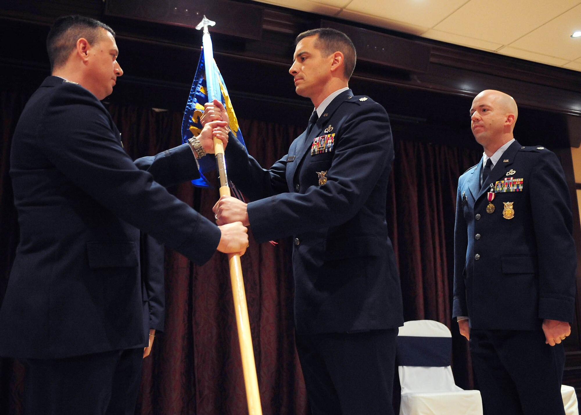 Col. Johnathan Hughes, 421st Air Base Group commander, recieves the guidon from Lt. Col. Bradford Buckman, the new 421st Civil Engineer Sqauadron commander, as Lt. Col. Mark Laudenslager, the outbound commander, looks on during the change of command ceremony at the Menwith Hill Base Club, June 20, 2011.