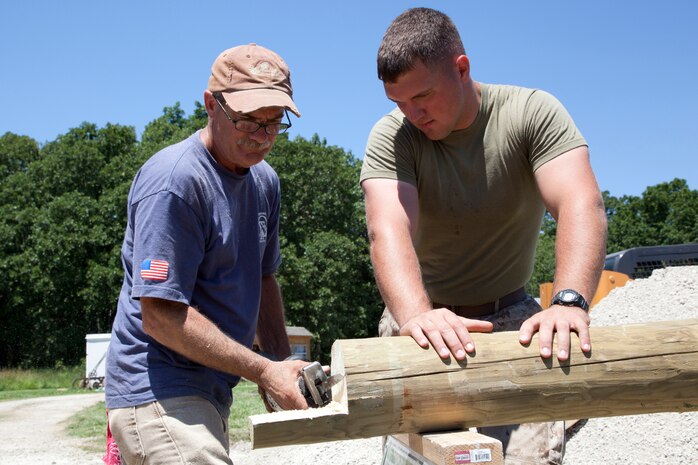 Cpl. Matthew J. Light, a granadier with Company I, 3rd Battalion, 24th Marine Regiment, Special Purpose Marine Air Ground Task Force Marine Week holds an 8-foot cedar log while a civilian volunteer cuts a notch in the log so it can be used for a fence. Marines volunteered with the Multiple Sclerosis Society to make Dauwalters farm more accessible from her wheelchair. Marine Week provides an opportunity to increase public awareness of the Marine Corps' value to our nation's defense and to preserve and mature the Corps' relationship with the American people. ::r::::n::