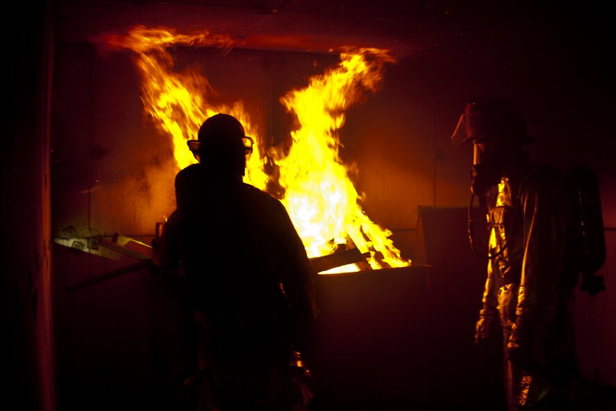 Two firefighters from the 23rd Civil Engineer Squadron stand near a flame as the room’s heat rises to nearly 1,000 degrees Celsius during training at Moody Air Force Base, Ga., June 24, 2011. The firefighter’s suits are designed to withstand extreme heat to keep them safe. (U.S. Air Force photo by Airman 1st Class Nicholas Benroth/Released)