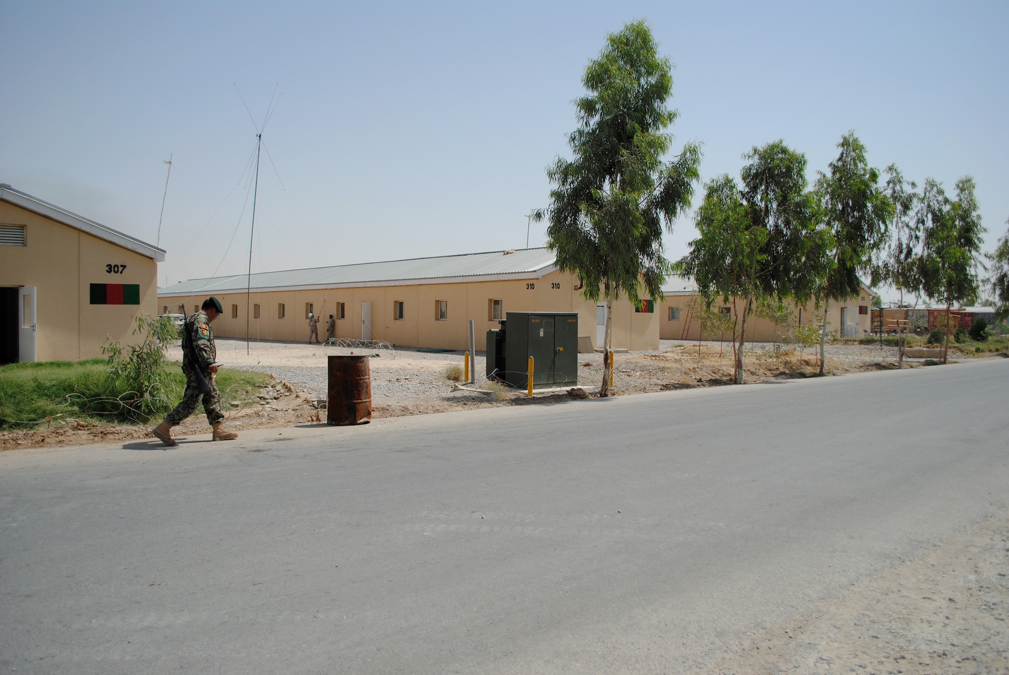 An Afghan National Army soldier walks past several buildings now officially in Afghan possession on Jun. 25, 2011, at Camp Hero, Kandahar, Kandahar province, Afghanistan.  NATO Training Mission-Afghanistan's Infrastructure Training and Advisory Group plans to turn 17 buildings over to Afghan control on Camp Hero.  Each Afghan-maintained building will display a painted Afghan flag.  (U.S. Air Force photo by Tech Sgt. Adrienne Brammer)
