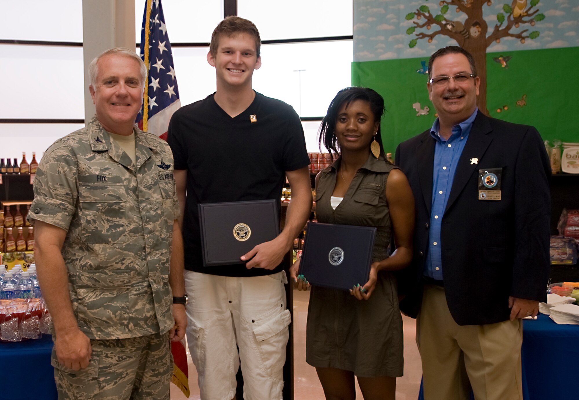 Col. Kevin Fox, 99th Mission Support Group commander, and Mr. Richard Means (right), Nellis Commissary store director, stand with Dallas Tueller and Kirstie McTear, two of the four scholarship recipients, during the Scholarships for Military Children ceremony, Nellis Air Force Base, Nev., June 24, 2011. The four scholarship recipients were selected based on academic merit, the quality of their essays, and their participation in extracurricular and volunteer activities. (U.S Air Force photo by Senior Airman Stephanie Rubi / Released)
