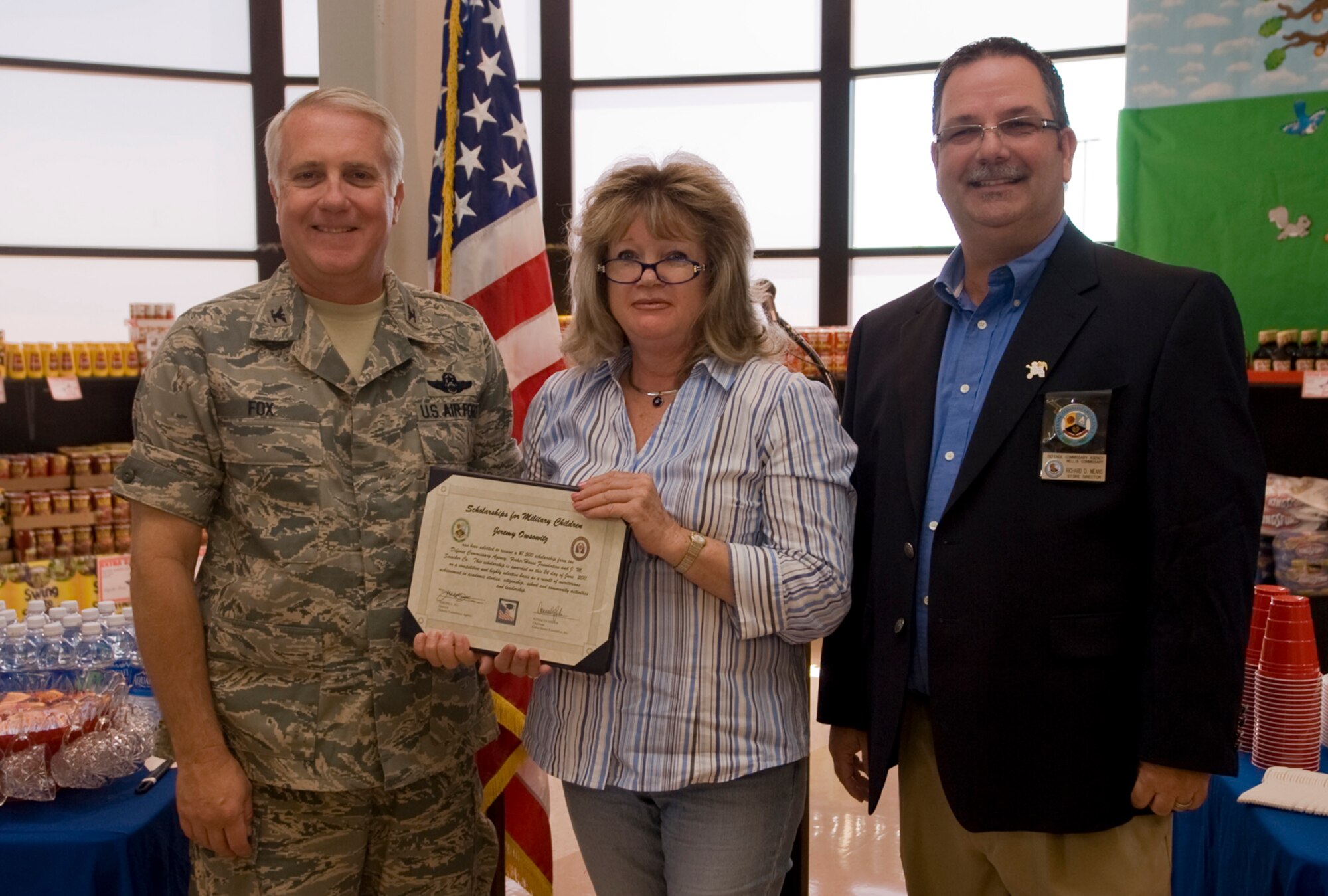 Col. Kevin Fox, 99th Mission Support Group commander, and Mr. Richard Means (right), Nellis Commissary store director, present a scholarship to Felicity Wsowitz, mother of Jeremy Wsowitz, the scholarship recipient, during the Scholarships for Military Children ceremony, Nellis Air Force Base, Nev., June 24, 2011.  Mr. Wsowitz is one of four students to receive a scholarship, all of whom were selected based on academic merit, the quality of their essays, and their participation in extracurricular and volunteer activities. (U.S Air Force photo by Senior Airman Stephanie Rubi / Released)

