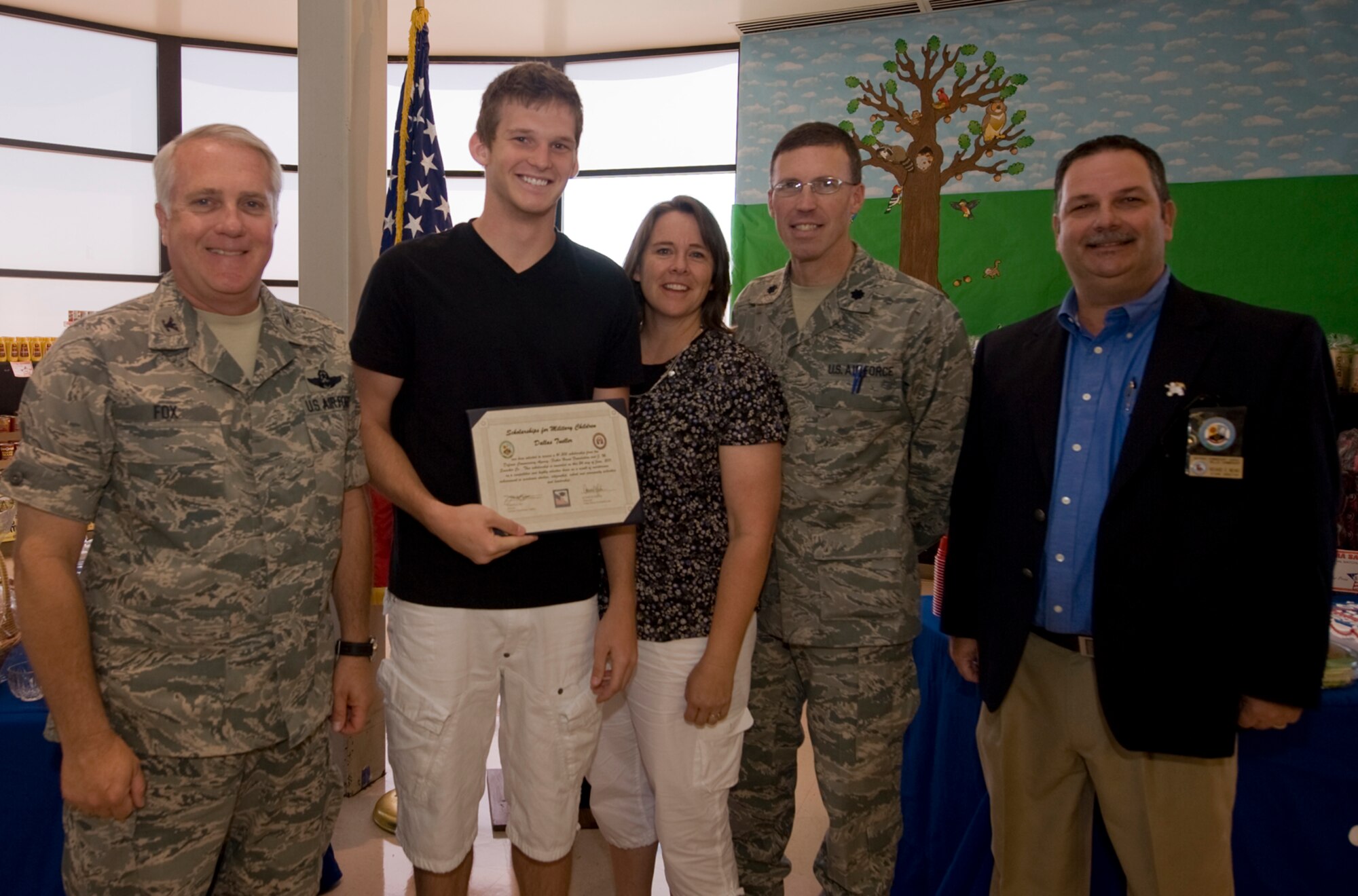 Col. Kevin Fox, 99th Mission Support Group commander, and Mr. Richard Means (right), Nellis Commissary store director, present a scholarship to Dallas Tueller, son of Camille Tueller and Lt. Col. Stephen Tueller, during the Scholarships for Military Children ceremony, Nellis Air Force Base, Nev., June 24, 2011. Mr. Tueller is one of four students to receive a scholarship, all of whom were selected based on academic merit, the quality of their essays, and their participation in extracurricular and volunteer activities.  (U.S Air Force photo by Senior Airman Stephanie Rubi / Released)

