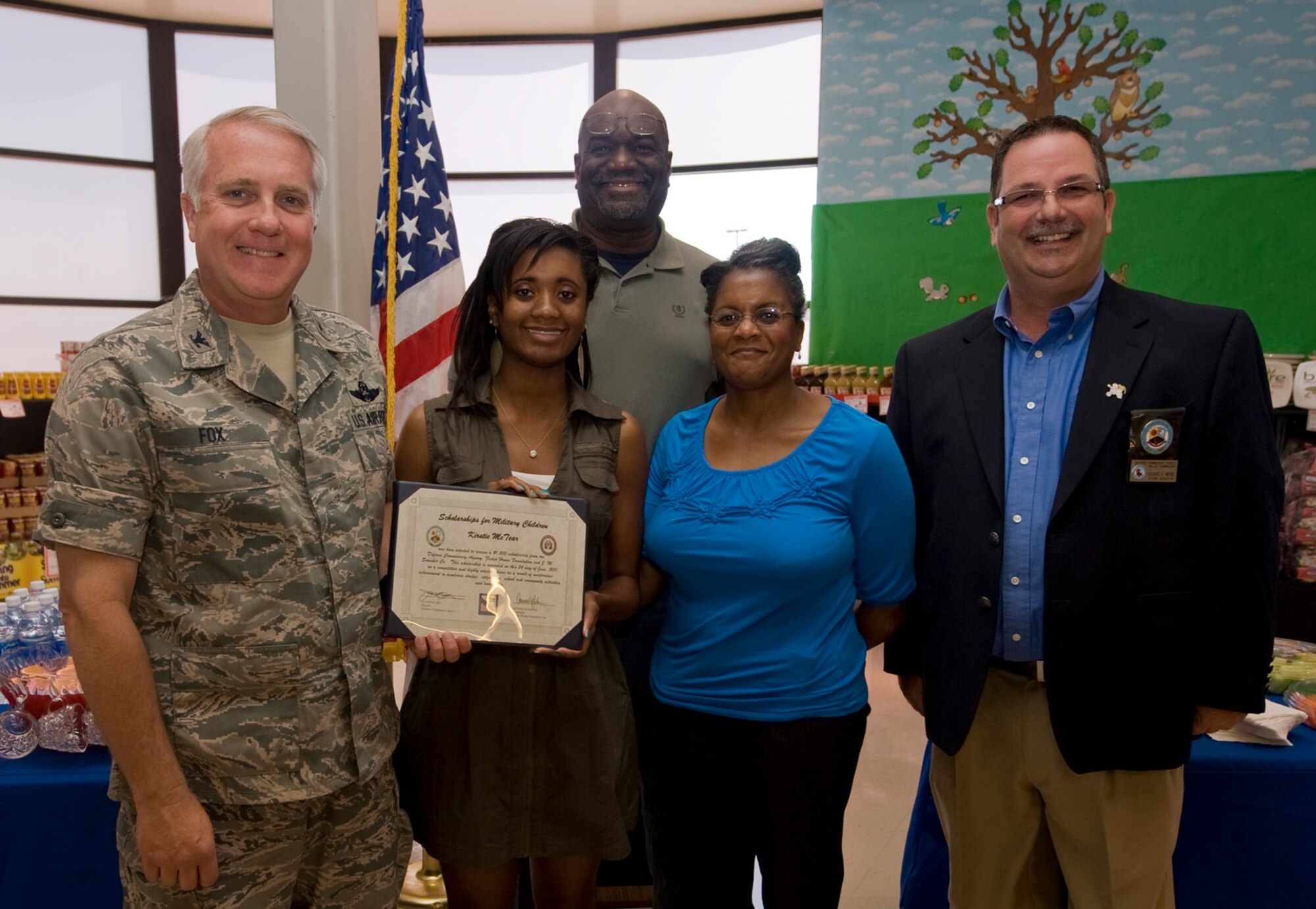 Col. Kevin Fox, 99th Mission Support Group commander, and Mr. Richard Means (right), Nellis Commissary store director, present a scholarship to Kirstie McTear, daughter of Donelle McTear and retired Tech. Sgt. Curtis McTear, during the Scholarships for Military Children ceremony, Nellis Air Force Base, Nev., June 24, 2011.  Miss McTear is one of four students to receive a scholarship, all of whom were selected based on academic merit, the quality of their essays, and their participation in extracurricular and volunteer activities.  (U.S Air Force photo by Senior Airman Stephanie Rubi / Released)

