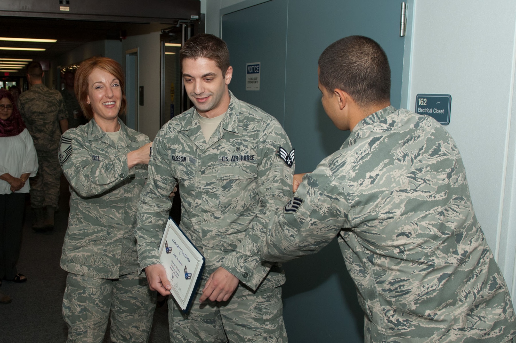 HANSCOM AIR FORCE BASE, Mass. - Airman 1st Class Todd Olsson (middle), 66th Medical Squadron, gets stripes tacked on by Chief Master Sgt. Laura Noel, Electronic Systems Center interim command chief, and Staff Sgt. Andre Olaciregui, his supervisor, at the 66th Medical Squadron clinic June 23. Airman Olsson was selected as Senior Airman Below the Zone for the second quarter. (U.S. Air Force photo by Rick Berry)