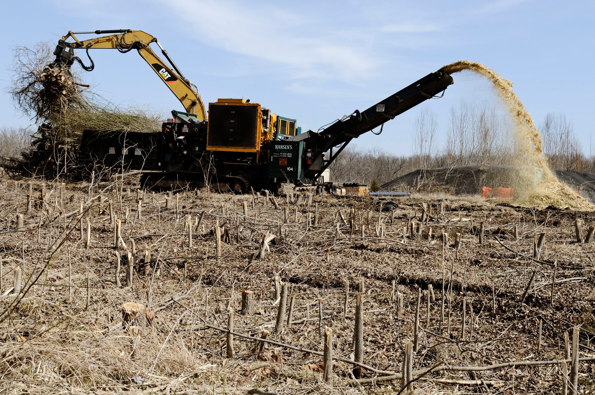 An excavator drops trees into an industrial chipper after they were removed from a landfill site Mar. 1, 2011 at Scott Air Force Base, Ill. The base landfill that operated from the 1940's until 1976 is being capped as part of a $20 million project. The 36 acre landfill engineered capping will consist of a one-foot thick gravel layer for methane gas collection, a geosynthetic liner to cover all of the landfill waste and prevent future contact with the waste, a drainage layer to funnel rainwater off of the liner, and two feet of clean soil to serve as a protective layer for the liner and to support vegetative growth. As part of the landfill capping project, the first phase is to remove the trees that have grown on top of the landfill. Capping the former base landfill is part of the Environmental Restoration Program efforts to meet the Air Force's goal of having remedies in place at contaminated sites by the end of 2012. (U.S. Air Force Photo/Staff Sgt. Brian J. Valencia)