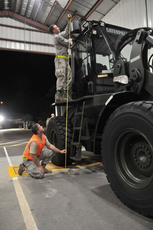 Staff Sgt. Andy Clyde (bottom), joint inspector from the 437th Aerial Port Squadron, and Senior Airman Michael Speaks, increment monitor from the 437 APS, measure the height of a Caterpillar loader during the mobility exercise Feb. 24 at Joint Base Charleston. The measurement ensured the equipment would fit into a C-17. (U.S. Air Force photo/Airman 1st Class Jared Trimarchi)