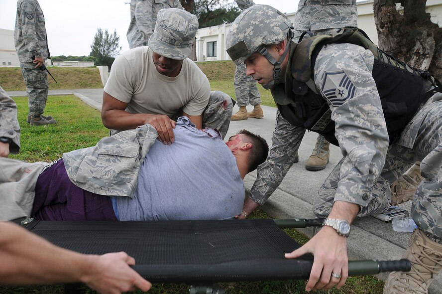 Senior Airman Covey Little, 18th Communications Squadron network control center technician, lifts a simulated victim while Master Sgt. Armando Alvarez, 18th Communications Squadron network control center superintendent, slides a litter under the victim during the local operational readiness exercise at Kadena Air Base, Japan March 2. This scenario tested the Airmens’ ability to secure the area and provide self-aid and buddy care after a simulated bomb attack. (U.S. Air Force photo/ Staff Sgt. Darnell T. Cannady)