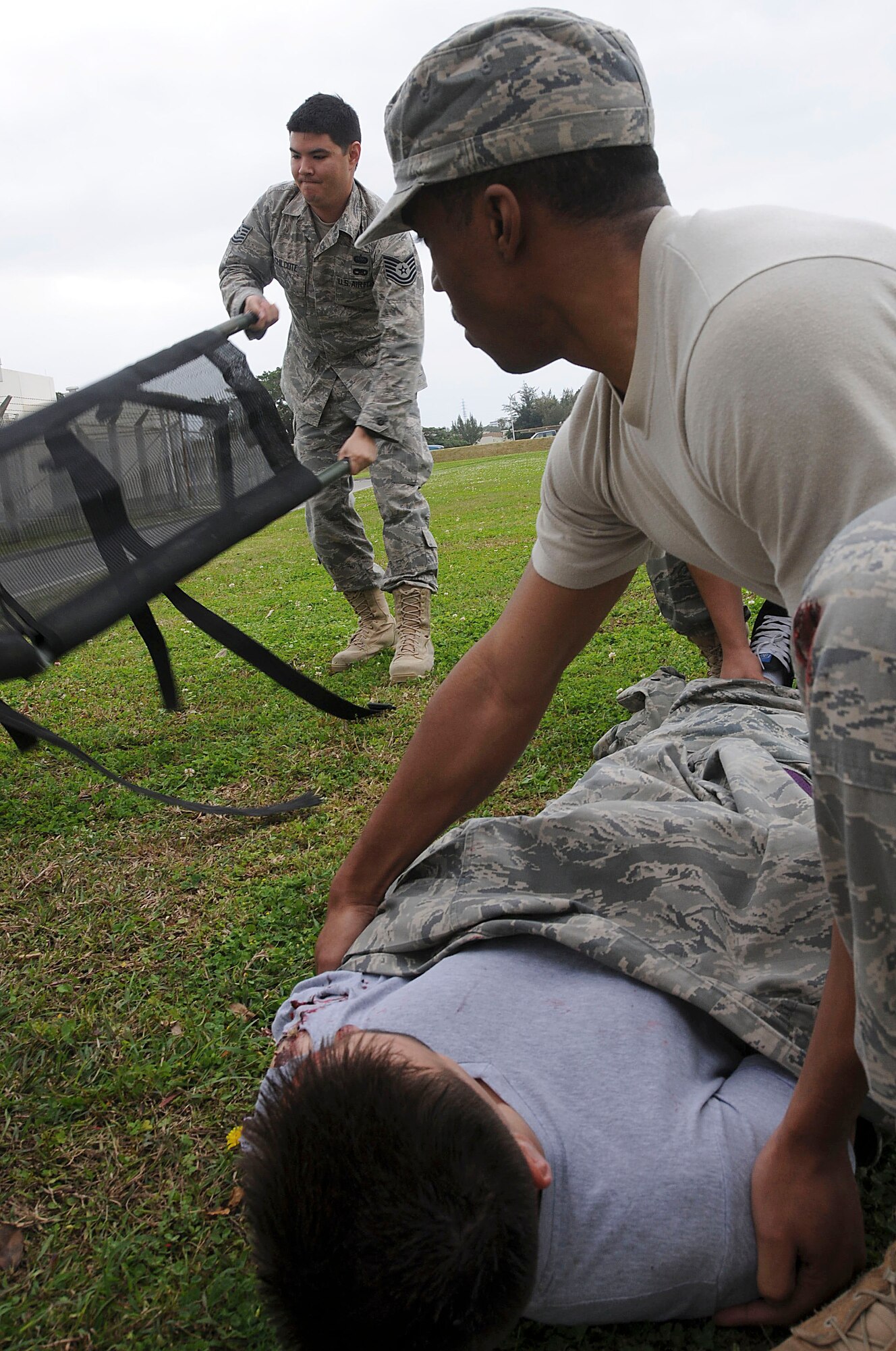 Senior Airman Covey Little, 18th Communications Squadron network control center technician, applies pressure to the arm of a simulated victim while Tech. Sgt. Jeremy Chilcote, also with the 18th Communications Squadron network control center, prepares the litter for transport during the local operational readiness exercise at Kadena Air Base, Japan March 2. This scenario tested the Airmens’ ability to secure the area and provide self-aid and buddy care after a simulated bombing attack. (U.S. Air Force photo/ Staff Sgt. Darnell T. Cannady)