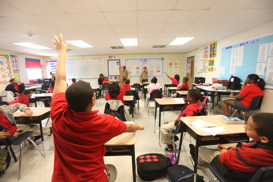 Students raise their hands eagerly waiting to be called upon to ask questions at Sarah T. Reed Elementary School March 2.  Marines read to the students as part of Dr. Seuss Day celebration.