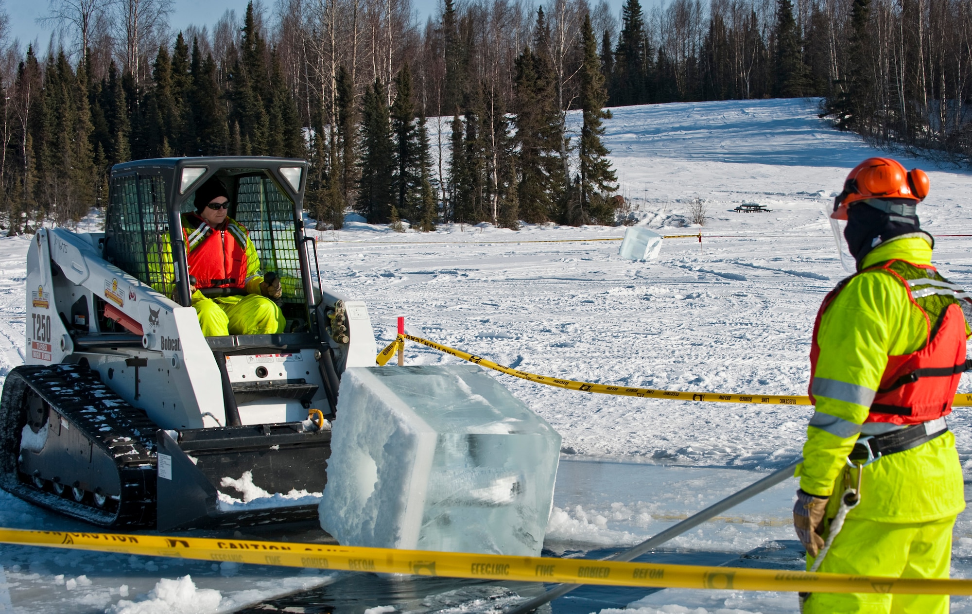 JOINT BASE ELMENDORF-RICHARDSON, Alaska -- Tech. Sgt. Andrew Perrin, 611th Civil Engineer Squadron, looks on as Tech. Sgt. Lucas Clark, 611th CES, uses a Bobcat to push a block of ice back into the water March 1 at JBER's Six-Mile Lake during the annual Ice Operations Exercise. Approximately a combined 60 members from the 611th CES, U.S. Coast Guard, the Navy's Supervisor of Salvage, Alaska Department of Environmental Conservation and the Alaska Chadux Corporation participated in the annual exercise, where participants practice various oil spill clean-up drills in preparation if there was ever an event here in Alaska. (U.S. Air Force photo by Senior Airman Christopher Gross)