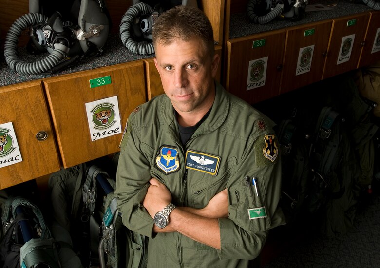 EMERGENCY IN THE TALON - Major Cory Christopher poses in front of G-suits and helmets. (Photo by TSgt Samuel Bendet)