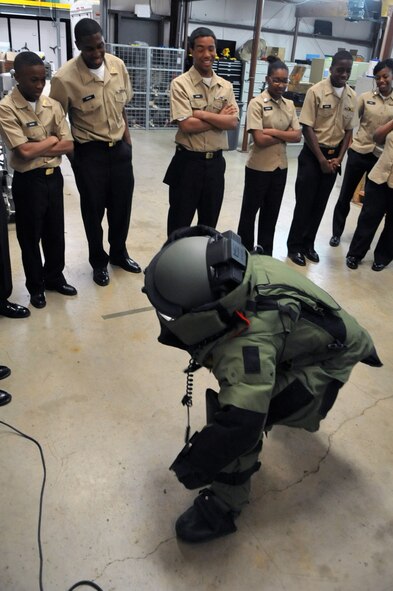 A Navy Junior Reserve Officer Training Corps cadet from Neville High School attempts to stand in an explosive ordnance disposal suit while her classmates watch, in the Explosive Ordnance Disposal garage on Barksdale Air Force Base, La., March 2. The cadets were briefed on the duties and responsibilities that EOD teams undertake at their home station and while deployed. Neville High School is located in Monroe, La. (U.S. Air Force photo/Airman 1st Class Micaiah Anthony)(RELEASED) 