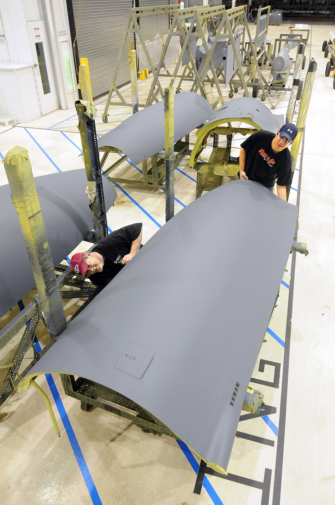 Painters Marlin Woods and Jason Blackburn, with the 551st CMMXS, remove masking from a B-52 side cowl.  The Paint Curing and De-Masking area is the "end of the line" for parts that are complete and ready to leave Bldg. 9001.  It is also one of many production areas that the 551st CMMXS has implemented One-Piece Modular Flow Assembly Line improvements at Bldg. 9001. (Air Force photos by Dave Faytinger)