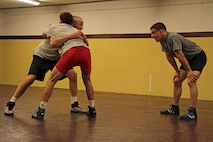 Dan Chandler uses All-Marine wrestler Sgt. Donavan Depatto, 26, from Monticello, Minn., to show 1st Lt. John Cox, 26, from Grand Haven, Mich., the proper technique to execute a step-around body lock in the University of Minnesota Gopher wrestling room March 4. The All-Marine athletes received one-on-one instruction after interacting with wrestlers competing in the state high school tournament. Chandler is a well-known international coach with multiple wrestling accolades at the World and Olympic levels.