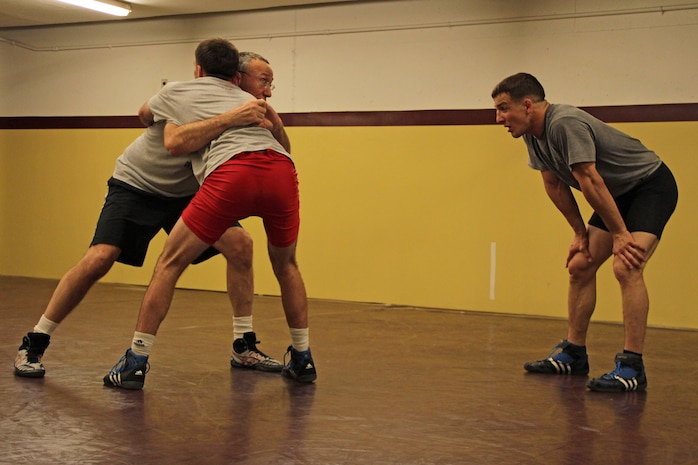 Dan Chandler uses All-Marine wrestler Sgt. Donavan Depatto, 26, from Monticello, Minn., to show 1st Lt. John Cox, 26, from Grand Haven, Mich., the proper technique to execute a step-around body lock in the University of Minnesota Gopher wrestling room March 4. The All-Marine athletes received one-on-one instruction after interacting with wrestlers competing in the state high school tournament. Chandler is a well-known international coach with multiple wrestling accolades at the World and Olympic levels.