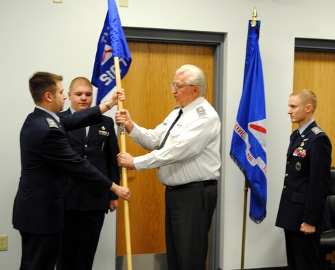 Outgoing commander Civl Air Patrol Maj. Adam Brandao passes the guidon to CAP Maj. Ed Olson while incoming commander CAP Maj. Andrew Treiman looks on. Cadet Calvin Mader served as the guidon bearer for the ceremony held March 1 at Malmstrom. (U.S. Air Force photo/Capt. Robert Wray)