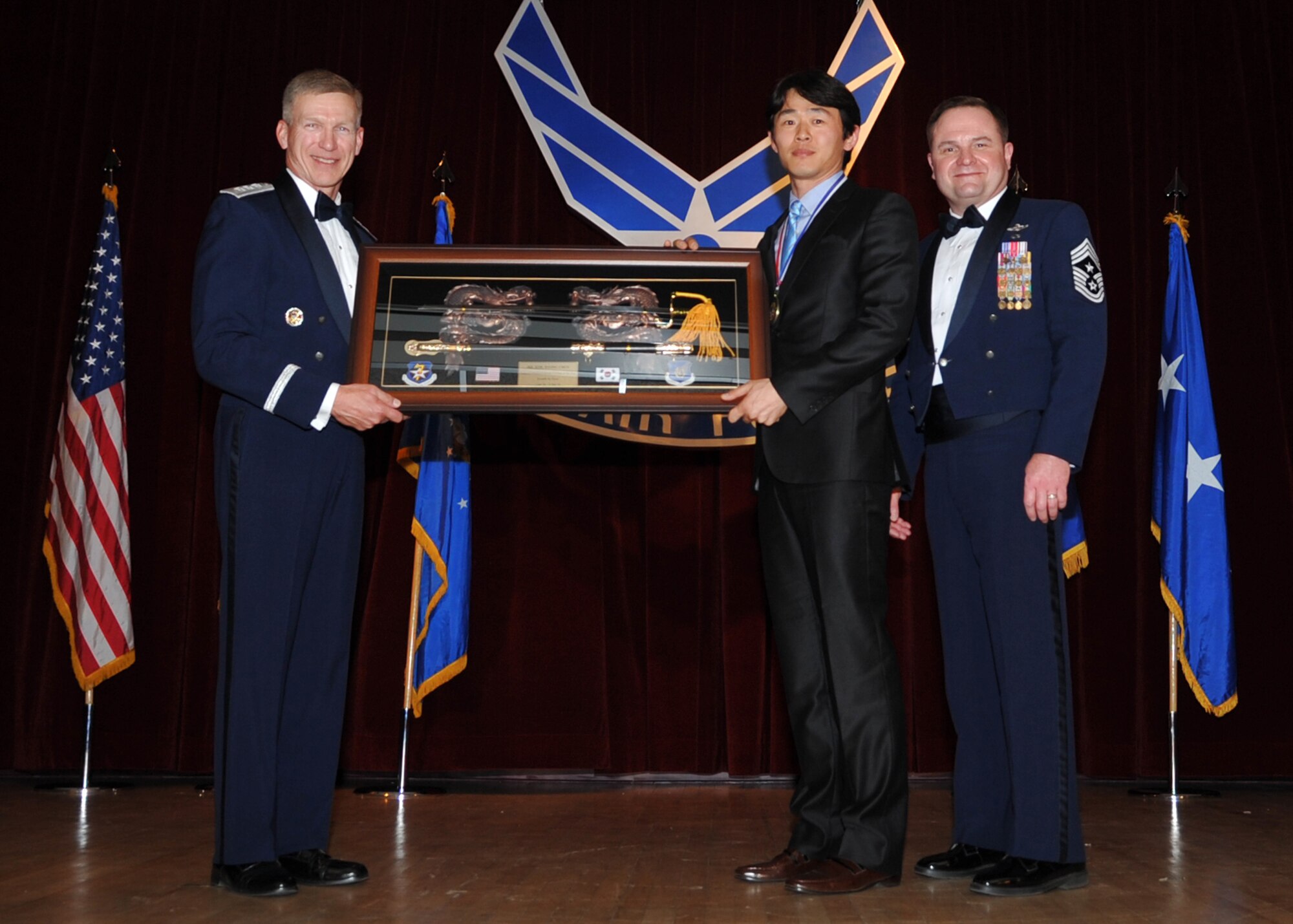 OSAN AIR BASE, Republic of Korea -- Lt. Gen. Jeffrey Remington, 7th Air Force commander, and Chief Master Sgt. Tom Baker, 7th AF command chief, present Kim Hyong-Chun, 8th Force Support Squadron material handler supervisor, with the 7th AF Category 1 Outstanding Civilian of the Year award at a banquet here Feb. 27. (U.S. Air Force photo/Senior Airman Evelyn Chavez)