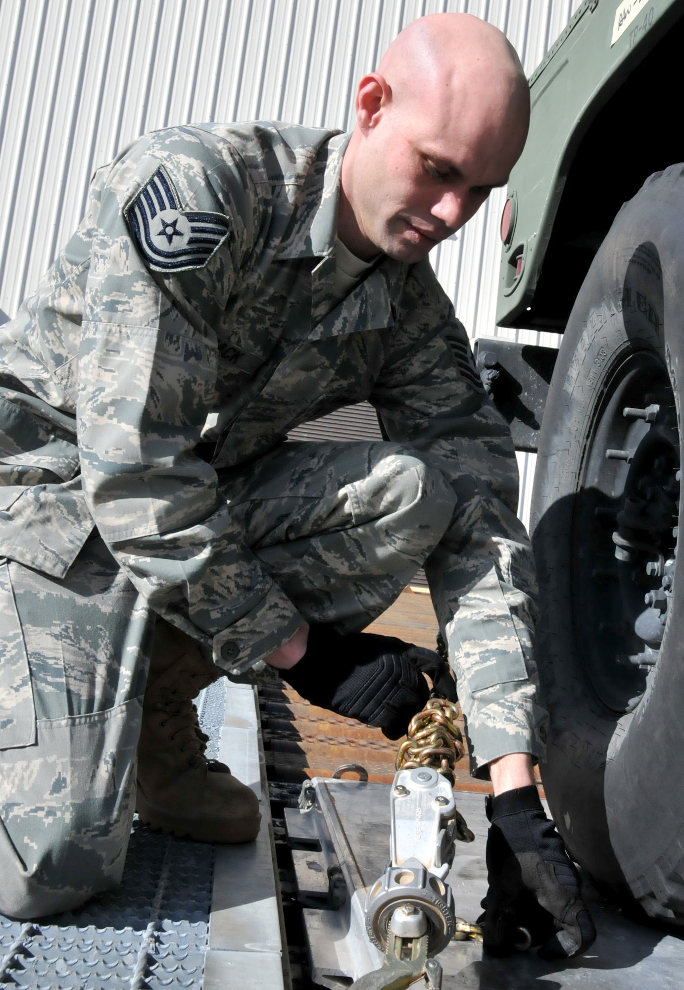 U.S. Air Force Tech. Sgt. John Carmack, 86th Aerial Port Squadron, McChord Field, Wash., tightens the chains on a pallet train during his squadron's monthly training exercise, March 5. Wrapping the chains ensures equipment safety during transit, specifically that the chains do not get stuck in the rails. (U.S. Air Force photo by Staff Sgt. Nicole Celestine/Released)