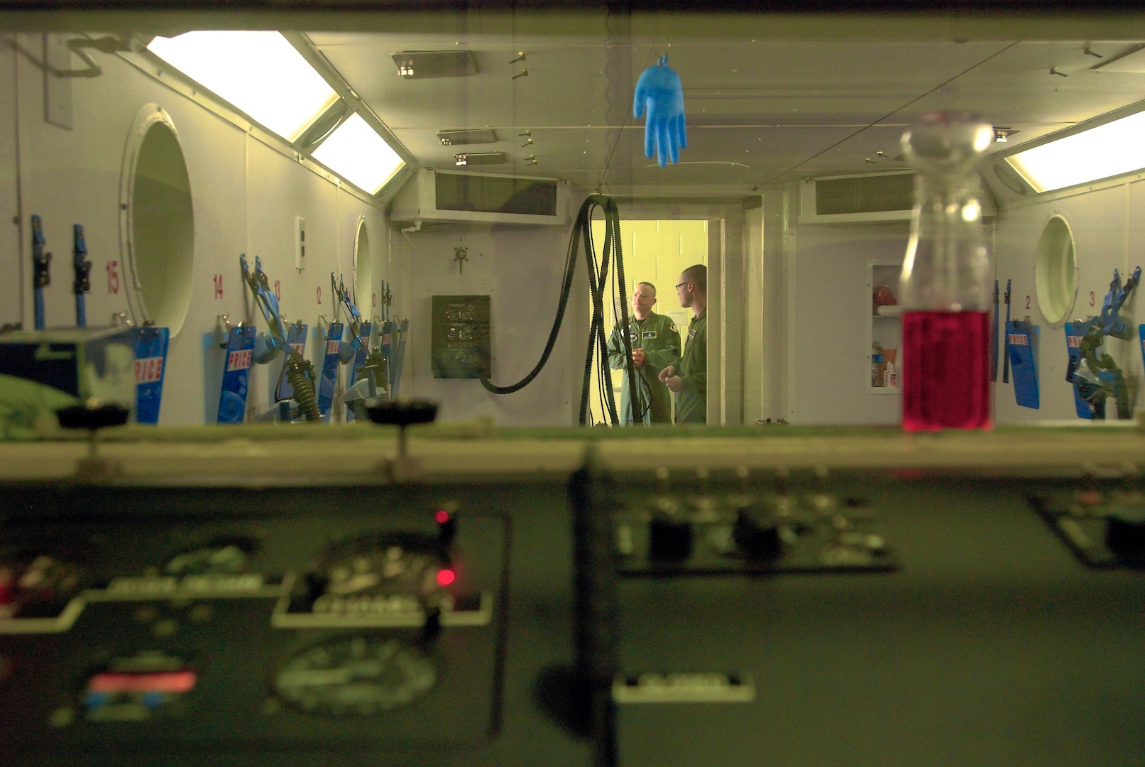 Part of the control panel and interior of the hypobaric chamber the 359th Aeromedical Squadron uses on Randolph Air Force Base, Texas, to test and train aircrew for hypoxia, or altitude sickness. The latex glove hanging from the ceiling expands and contracts with the changes in barometric pressure in the chamber, it?s used to show how gases in the human body also expand and contract with pressure changes. The bottle of red liquid has an inverted beaker in it and is used to show how pressure affects air and liquid in the inner ear. (U. S. Air Force photo/Brian McGloin)