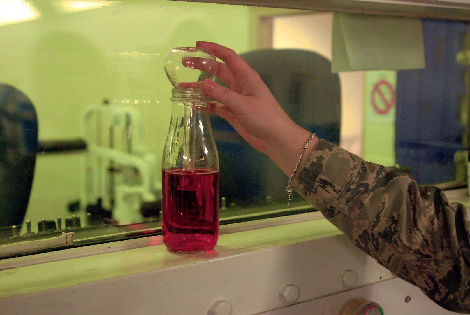 Airman 1st Class Kristen Coffey, 359th Aeromedical Squadron, aerospace operational physiology journeyman demonstrates the simple mechanism used to explain how fluid and air pressure equalize in the inner ear. The level of the red liquid in the jar ebbs and flows into the bulb of the inverted beaker as the barometric pressure in the chamber fluctuates. (U. S. Air Force photo/Brian McGloin)
