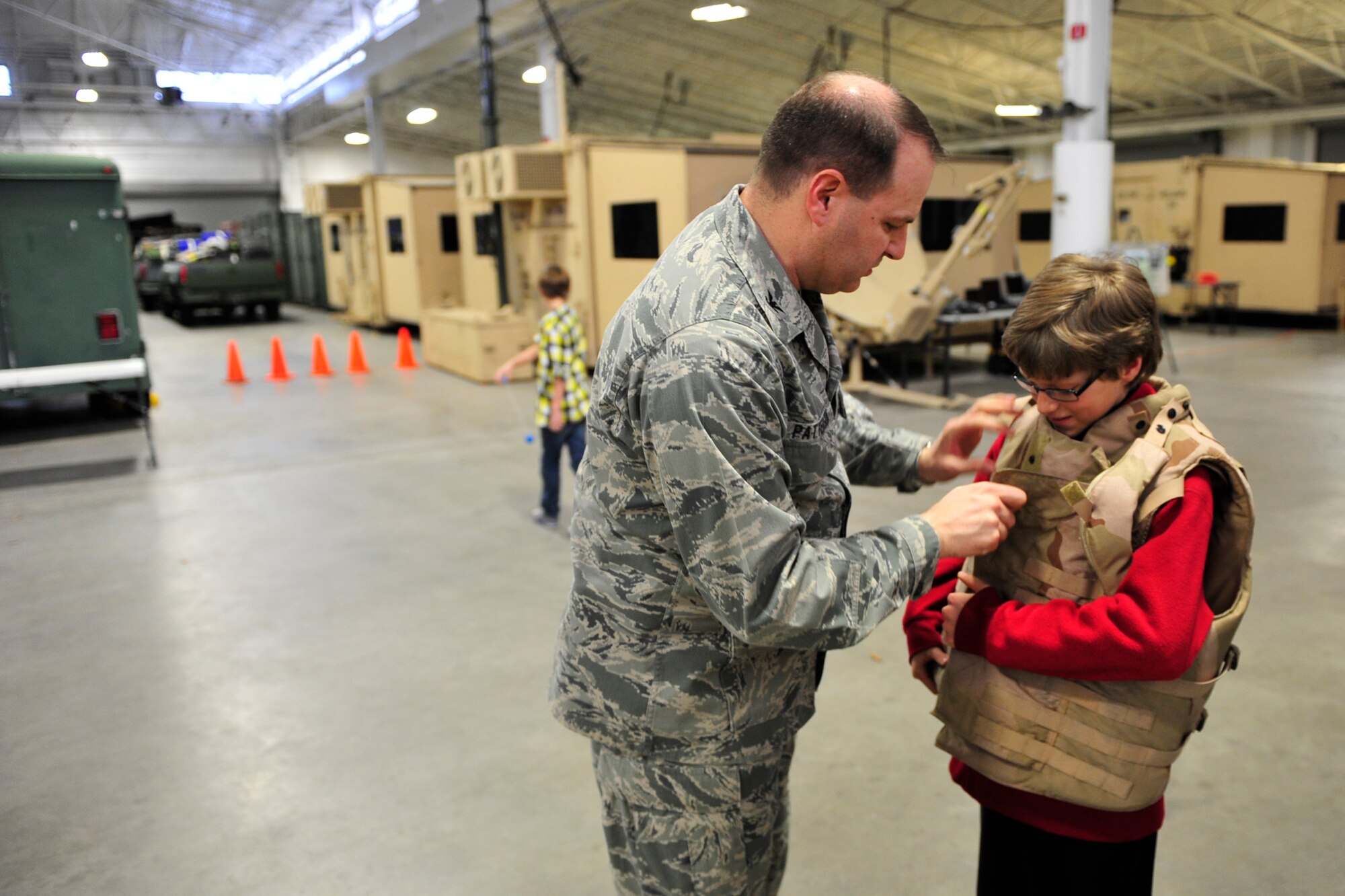 Col. Chris Patterson, 621st Contingency Response Wing commander, shows his 11-year-old his son Ross the proper way to close a body armor vest during the 621st CRW family open house at the Joint Base McGuire-Dix-Lakehurst, N.J. Global Reach Deployment Center here March 4.  The event included activities and food for the families alongside demonstrations of the specialized equipment used by the unit to provide emergency global mobility support to humanitarian crises and national defense operations. (U.S. Air Force photo/Tech. Sgt. Parker Gyokeres) (Released)
