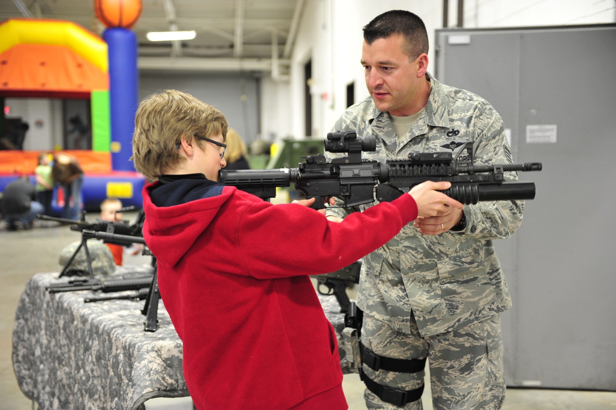 Ross Patterson, 11-year-old son of Col. Chris Patterson, 621st Contingency Response Wing commander, is instructed on the proper way of holding and aiming an M-4 carbine with an attached M203 grenade launcher by Tech. Sgt. Aaron White, 819th Global Support Squadron force protection supervisor, during the 621st CRW’s family open house at the Joint Base McGuire-Dix-Lakehurst, N.J. Global Reach Deployment Center March 4.  The event included activities and food for the families alongside demonstrations of the specialized equipment used by the unit to provide emergency global mobility support to humanitarian crises and national defense operations. (U.S. Air Force photo/Tech. Sgt. Parker Gyokeres) (Released)