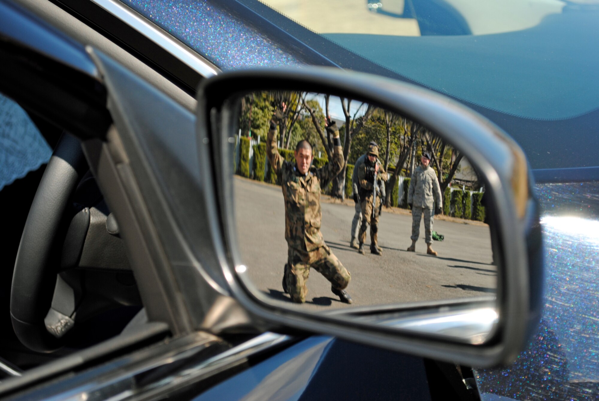 FUCHU AIR BASE, Japan -- Security guards from the Japan Air Self Defense Force are reflected in a vehicle's side mirror as they practice searching a suspicious vehicle and driver here Mar. 4 while Master Sgt. Eric Haeseker, 5th Air Force A7s manager, observes.  This was JASDF's second field training with U.S. Airmen supervising.  The security guards also covered team movement tactics, responding to near and far side ambush, and building entry procedures as they prepare to train other security guards once their new Base Defense Development and Training Squadron stands up in April. (U.S. Air Force photo/Capt. Will Powell)
