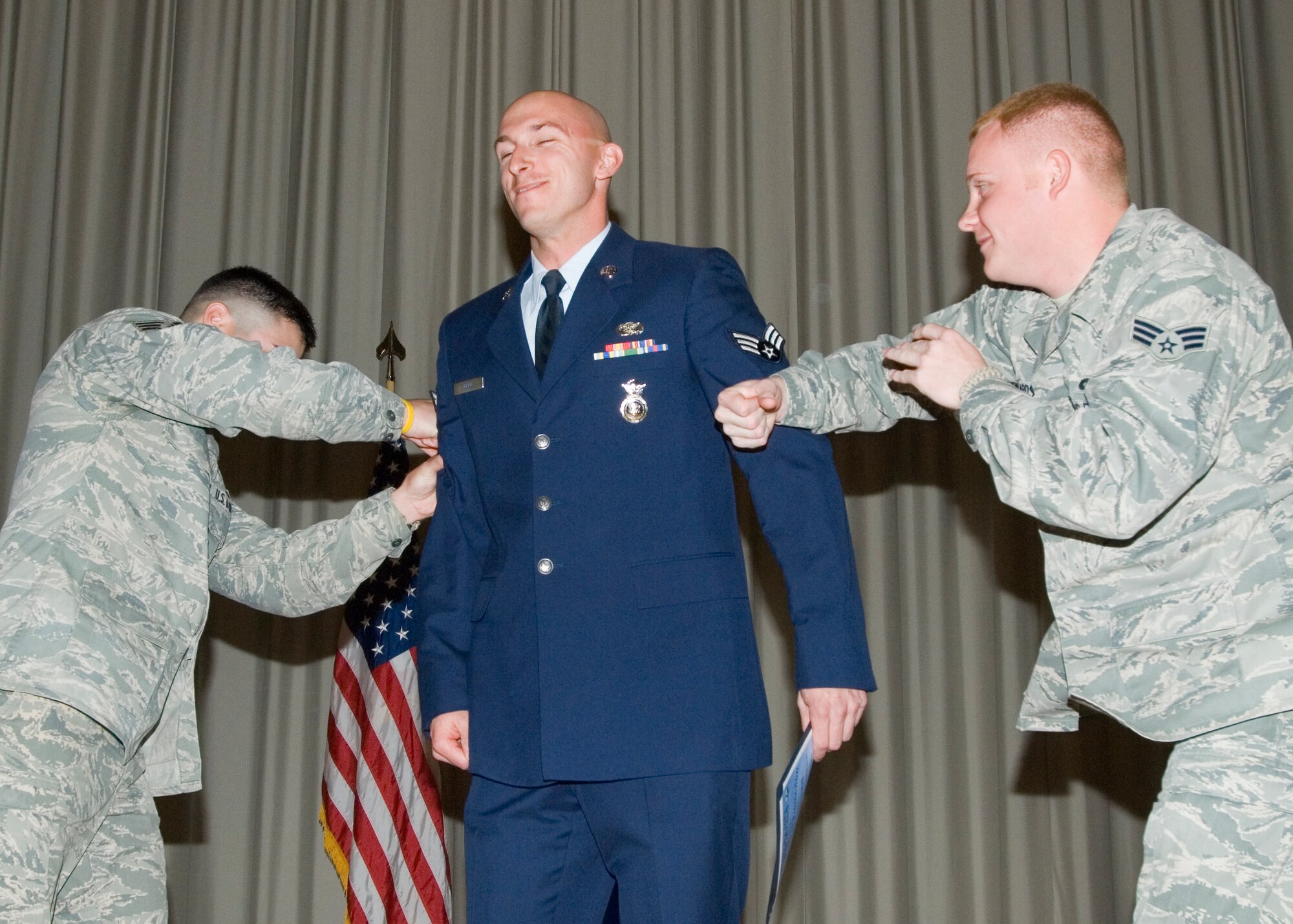Promotee Airman 1st Class Ryan Ball, 95th Security Forces Squadron, receives two right hooks from his co-workers Senior Airmen Aaron Mendoza (left) and Joe Edwards, both 95th SFS, as they help him pin on senior airman. Airman Ball, along with 17 others, was promoted in the Base Theater, Mar. 4, during the Team Edwards monthly promotion ceremony. (Air Force photo by Edward Cannon)