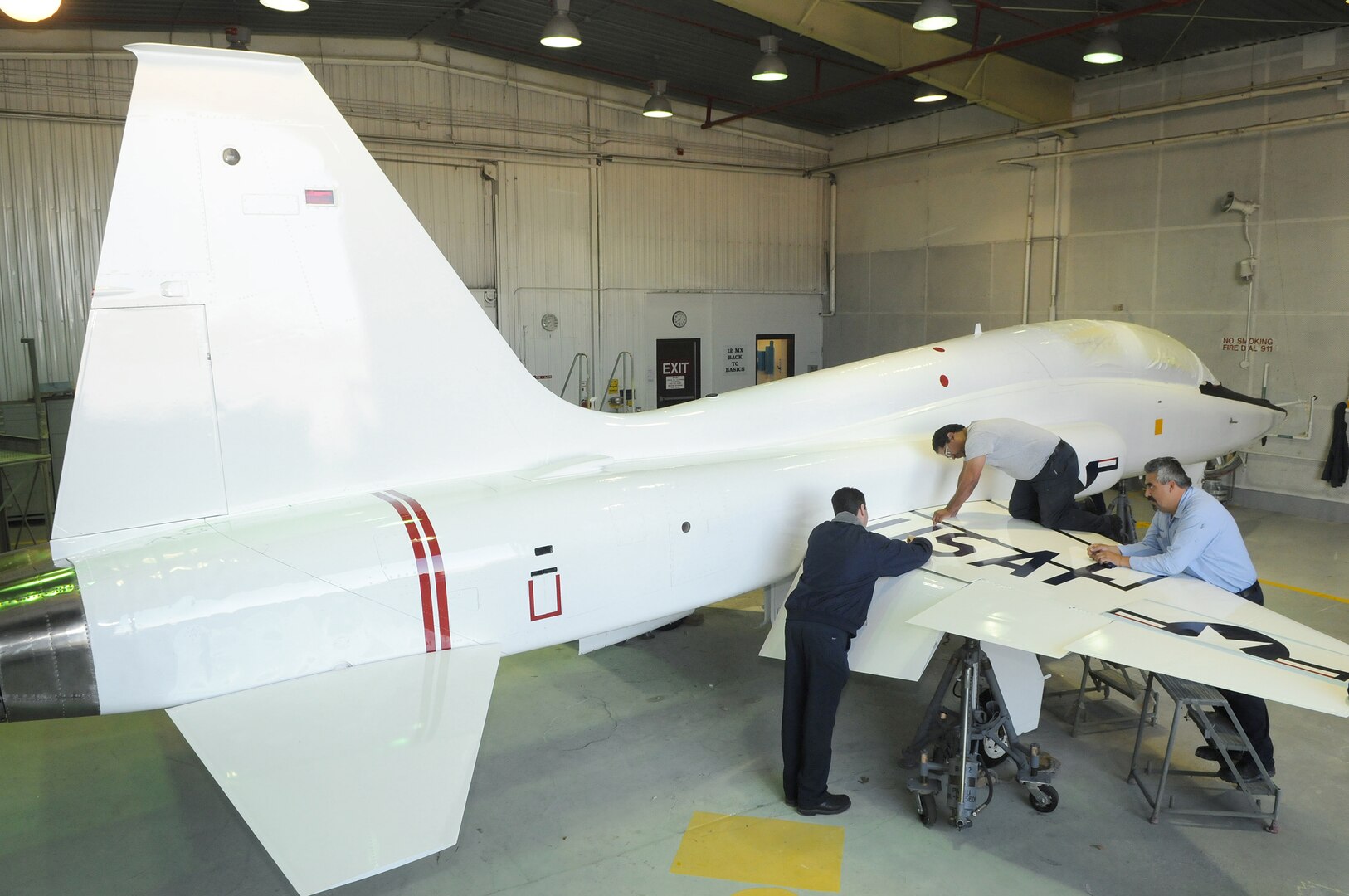 (Left to right) Neil Orlowski, Mario Tarin and Frank Garcia, 12th Flying Training Wing corrosion control, apply new decals to a T-38 Talon March 10. To mark the 50th anniversary of service, the aircraft has been repainted to match the colors used on the aircraft during the 1960s. (U.S. Air Force photo/David Terry)
