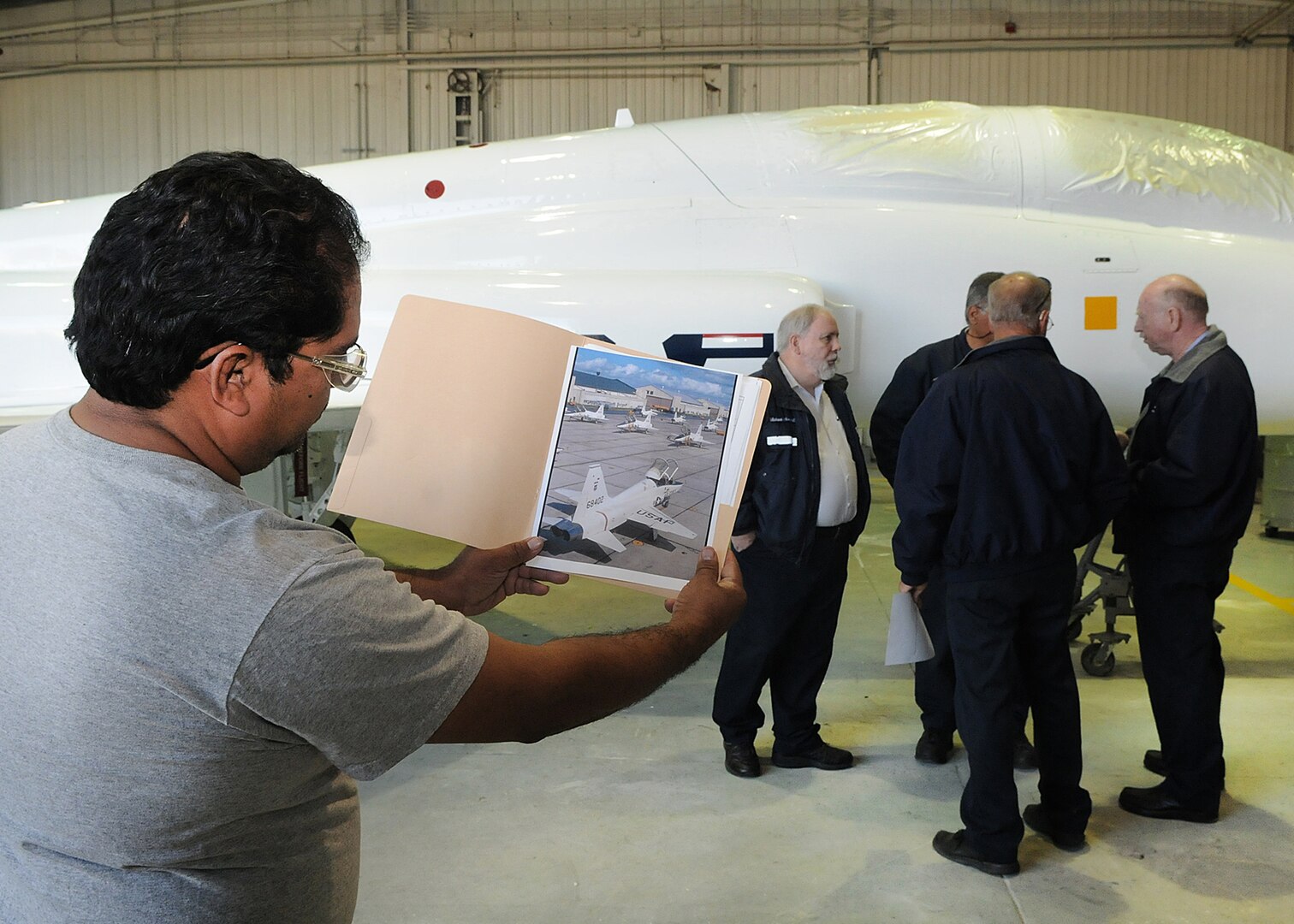 Mario Tarin, 12th Flying Training Wing corrosion control, compares a photo of a T-38 Talon, taken during the 1960s, with a T-38 Talon which was recently painted white in celebration of the 50th anniversary of the aircraft. Mr. Tarin and other aircraft painters with the 12th FTW, also applied 1960s style decals to the aircraft March 10, using the photograph to help duplicate the fifty-year-old aircraft markings. The T-38 marks 50 years of service March. 17. (U.S. Air Force photo/David Terry)