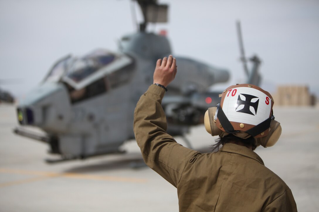 Cpl. Kelsey J. Canoy, a helicopter mechanic with Marine Light Attack Helicopter Squadron 169, communicates with the crew of an AH-1W Cobra using hand and arm signals at Camp Bastion, Afghanistan, March 11. “We do regular inspections after the aircraft has flown to make sure everything is still working properly,” said Canoy.::r::::n::::r::::n::::r::::n::