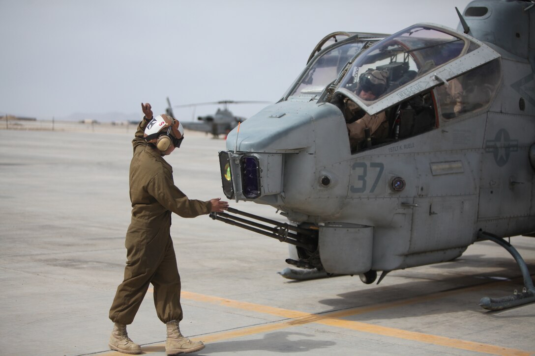 Cpl. Kelsey J. Canoy, a helicopter mechanic with Marine Light Attack Helicopter Squadron 169, communicates with the crew of an AH-1W Cobra using hand and arm signals at Camp Bastion, Afghanistan, March 11. “We do regular inspections after the aircraft has flown to make sure everything is still working properly,” said Canoy.::r::::n::::r::::n::::r::::n::
