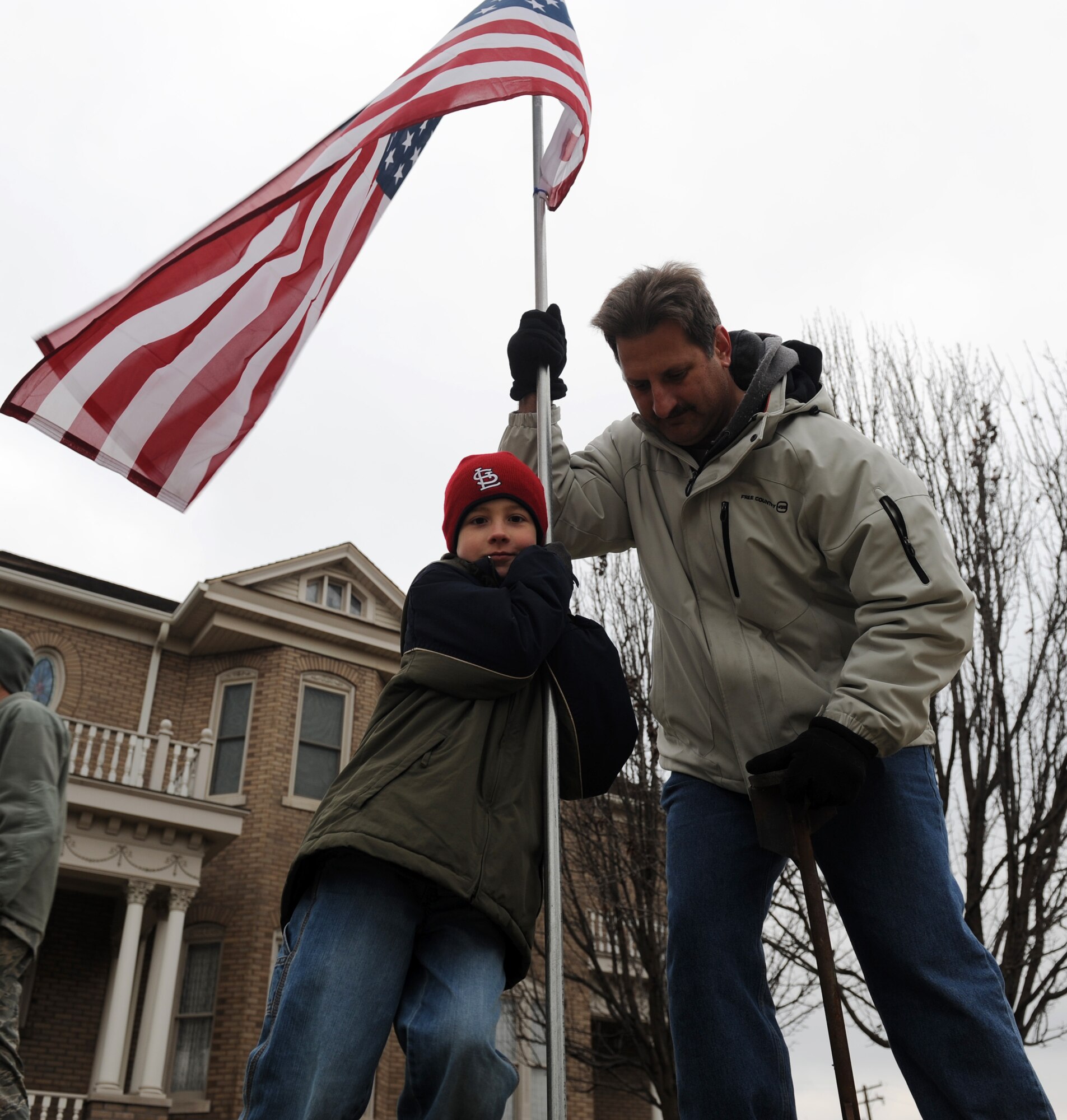 John McGinnis and his son, Conner, 9, place an American Flag along the procession route of Airman 1st Class Zachary Cuddeback March 10, 2011.  Airman Cuddeback and another Airman were killed March 2, 2011 when a man opened fire on a bus of U.S. Airmen at an airport in Frankfurt, Germany.  Airman Cuddeback will be laid to rest next to his grandfather at a cemetery in O'Fallon, Ill. (U.S. Air Force photo/Airman 1st Class Divine Cox)