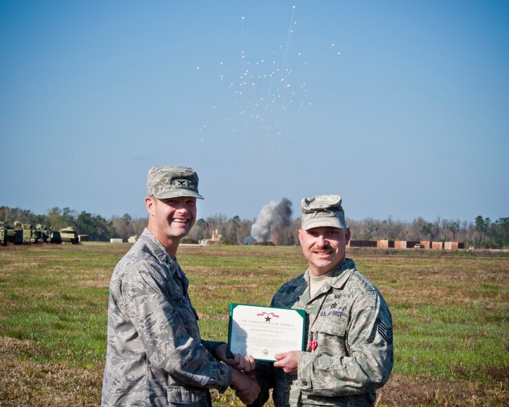 Tech. Sgt. Richard Schmidt, 35th Civil Engineer Squadron explosive ordnance disposal craftsman, receives a Bronze Star Medal presented by Col. Gary Henderson, 23rd Wing commander, as more than 1,000 30mm rounds go off March 11 at the Grand Bay Bombing and Gunnery Range, Moody Air Force Base, Ga.  During a recent deployment, Sergeant Schmidt served as an explosive ordnance device team leader in support of Operation Enduring Freedom. (U.S. Air Force photo/Staff Sgt. Jamal D. Sutter)(RELEASED)