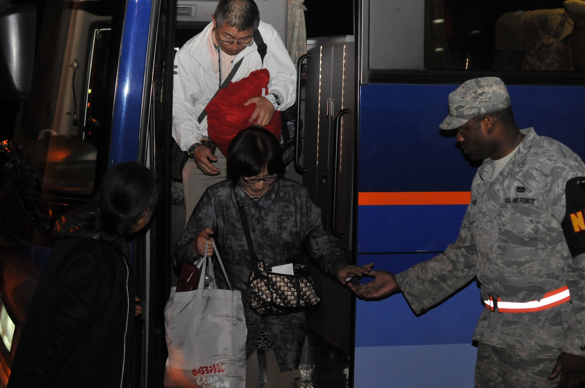 YOKOTA AIR BASE, Japan -- Mr. Suzuki Hideto, 374th Force Support Squadron recreational specialist, and Staff Sgt. Jason Holmes, 374th Civil Engineer Squadron, assist a passenger exiting a bus here March 11. The passengers arrived to the base after their commercial flights were diverted from Narita International Airport, Tokyo, Japan, due to an earthquake that struck near Tokyo. (U.S. Air Force photo/Airman John D. Partlow)