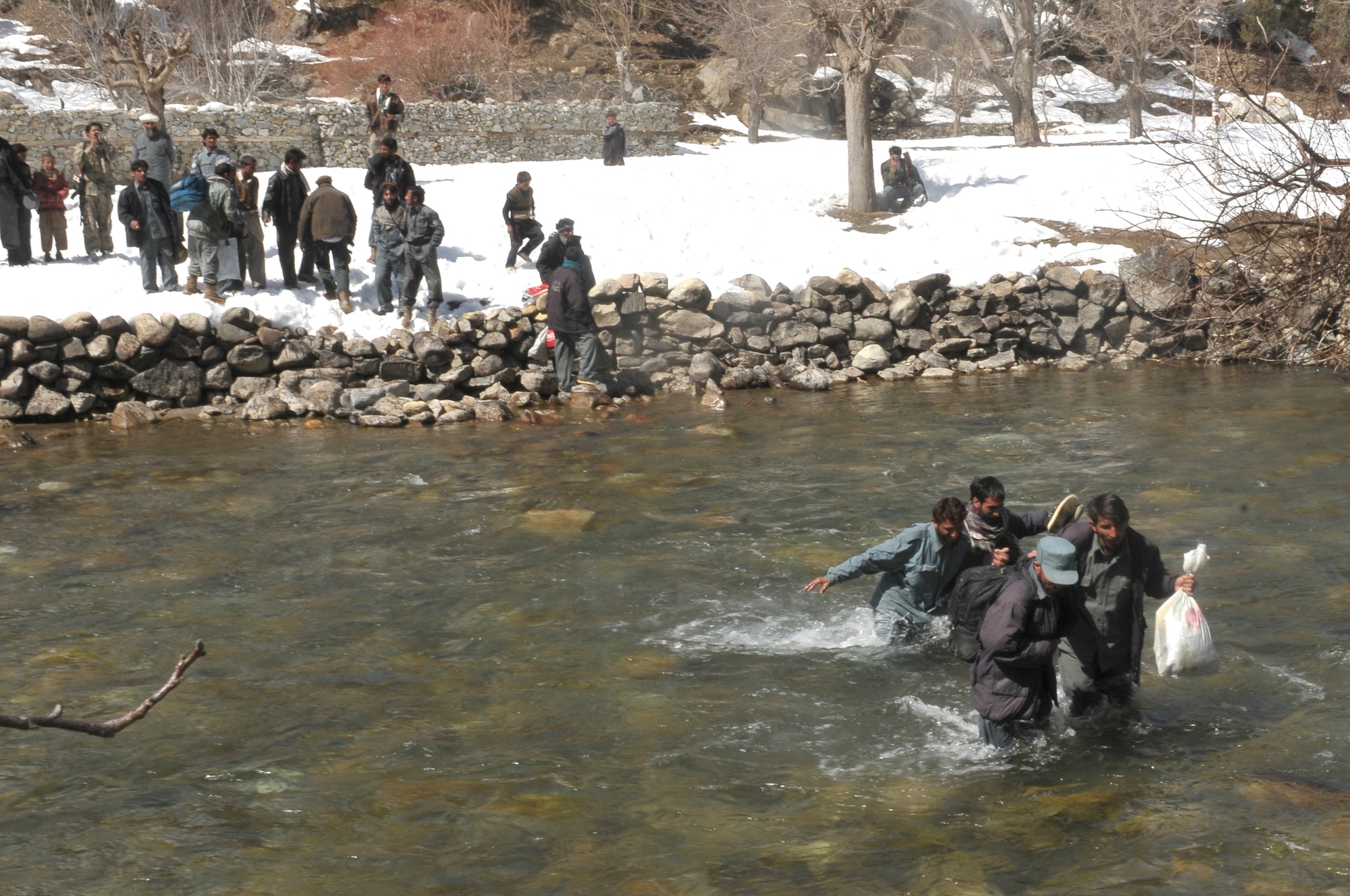 Barge Matal, Afghanistan – Afghan National Police troops wade through knee-high water to reach Mi-17 helicopters that will transport them back to their homes as part of a combat resupply mission in Barge Matal in the northern Kunar Valley March 10. The Afghan Air Force worked in cooperation with the Ministry of the Interior and coalition forces to complete the mission, using ten aircraft to deliver over 9,000 kilograms of weapons, ammunition and food to Afghan National Police stationed in the remote post that is seen as vital by Afghan officials due to its proximity to Pakistan and history of insurgent activity. Following the supply drop-off, forces loaded over 80 ANP bound for their respective homes following a three to six month deployment to the region. (U.S. Navy photo by Mass Communications Specialist 2nd Class Vladimir Potapenko).
