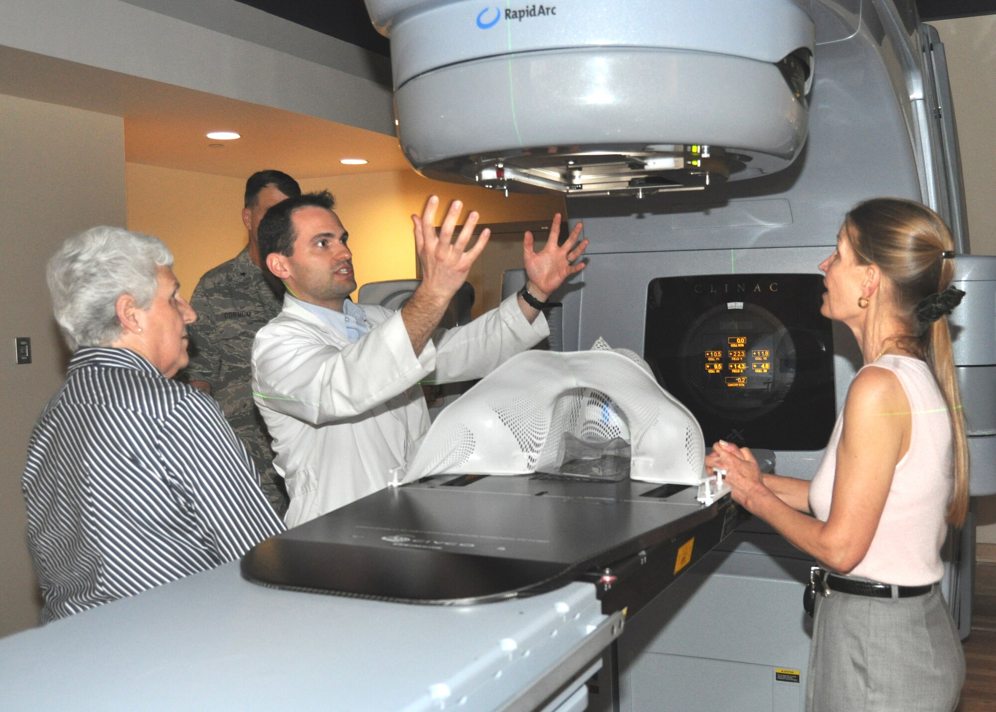 Maj. (Dr.) James Mitchell, center, 81st Medical Operations Squadron radiation oncologist, describes the operation of the radiation oncology clinic’s linear accelerator to Audrey Fisher, right, vice chairman of the Fisher House Foundation board of directors, during her Feb. 25 visit. Mrs. Fisher’s mother, Laura Randall, watches at left. They were accompanied by James Weiskopf, Fisher House Foundation vice president, as they visited the Keesler Fisher House where they accepted a $250 donation from the Keesler Spouses Club. The clinic was included in the visit since many Fisher House residents are patients or families of patients undergoing treatment there.  (U.S. Air Force photo by Steve Pivnick)